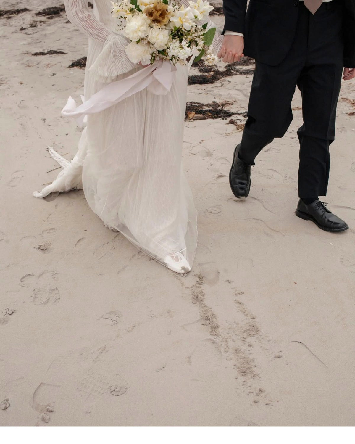 Bride and groom walking on a beach with a floral arrangement.