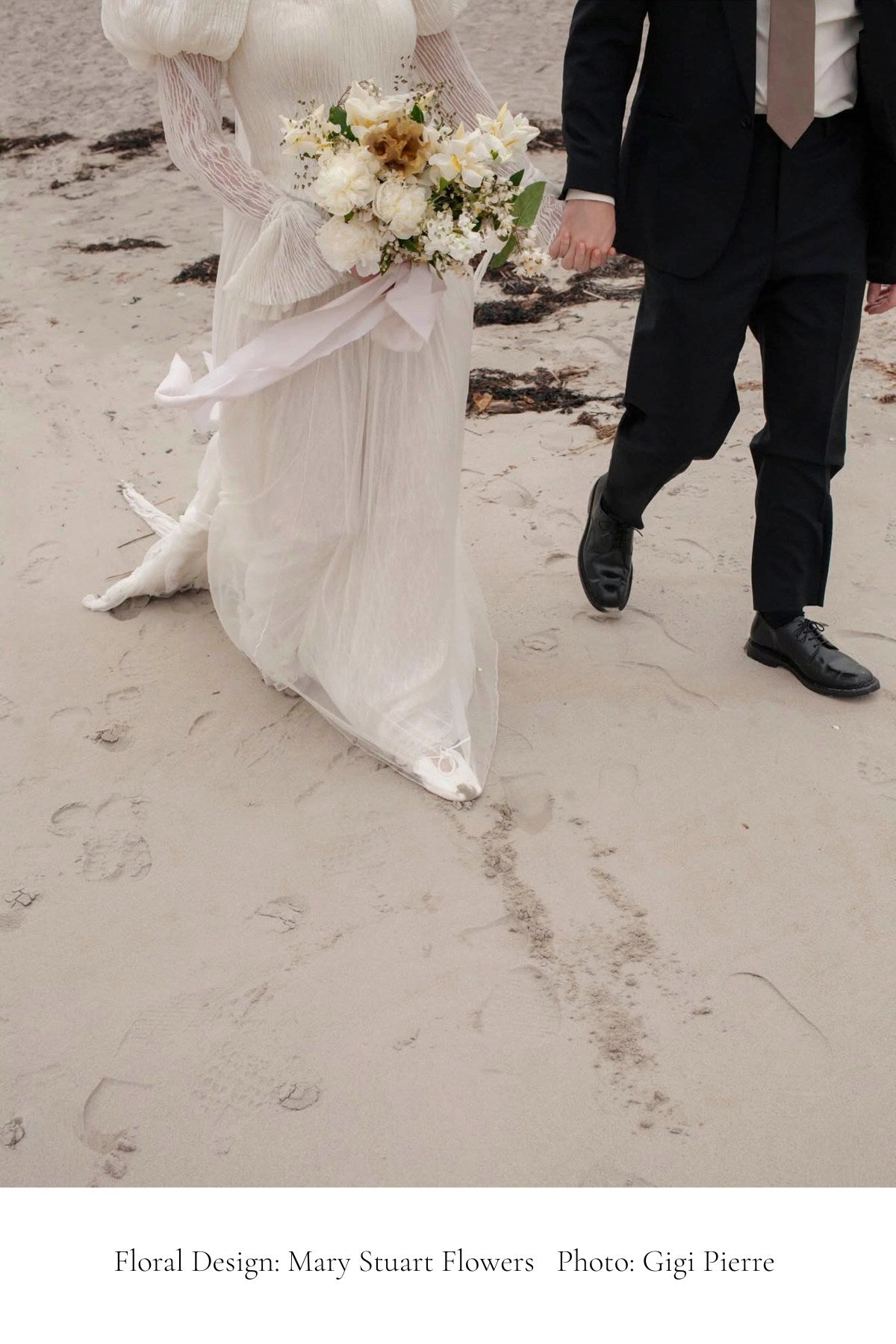 Bride and groom walking on a beach with a floral arrangement.