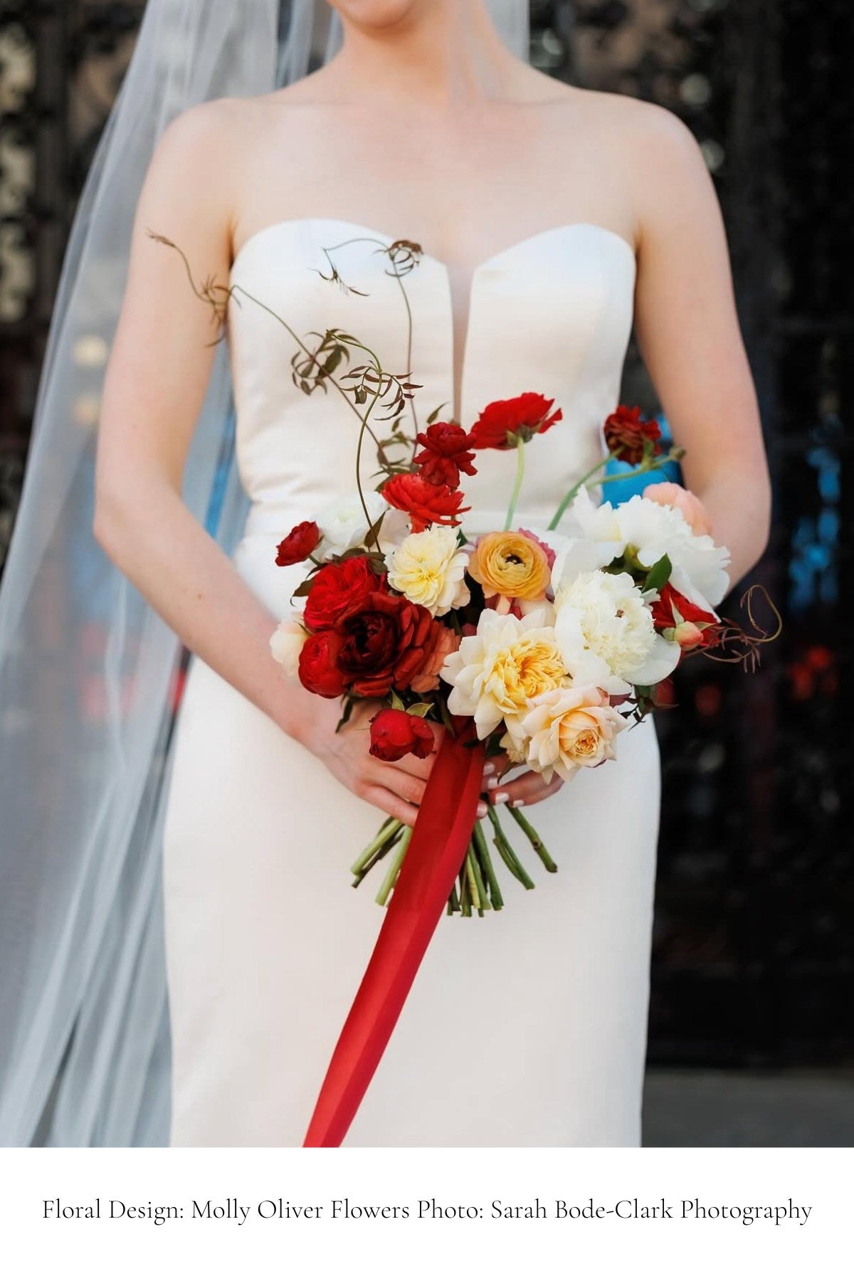 Bride holding a colorful bouquet with red silk ribbon with a blurred background