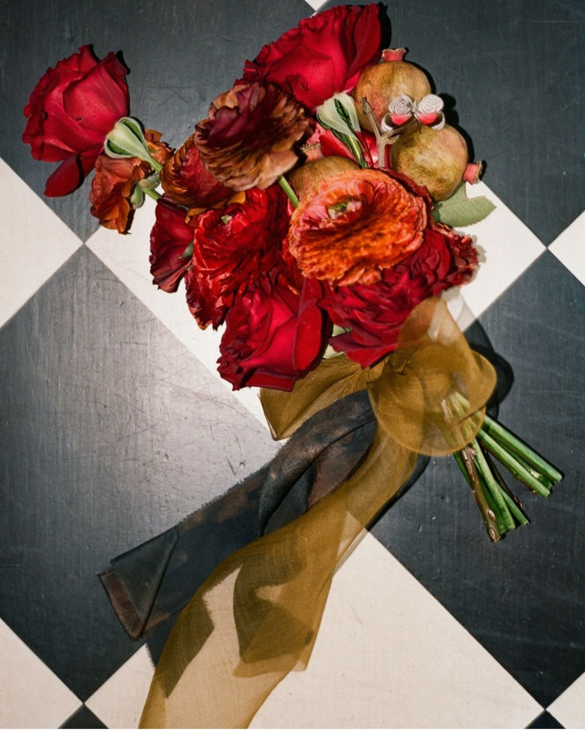 Bouquet of red and orange flowers by Nectar & Vessel with a silk & Willow ochre ribbon on a black and white checkered background.