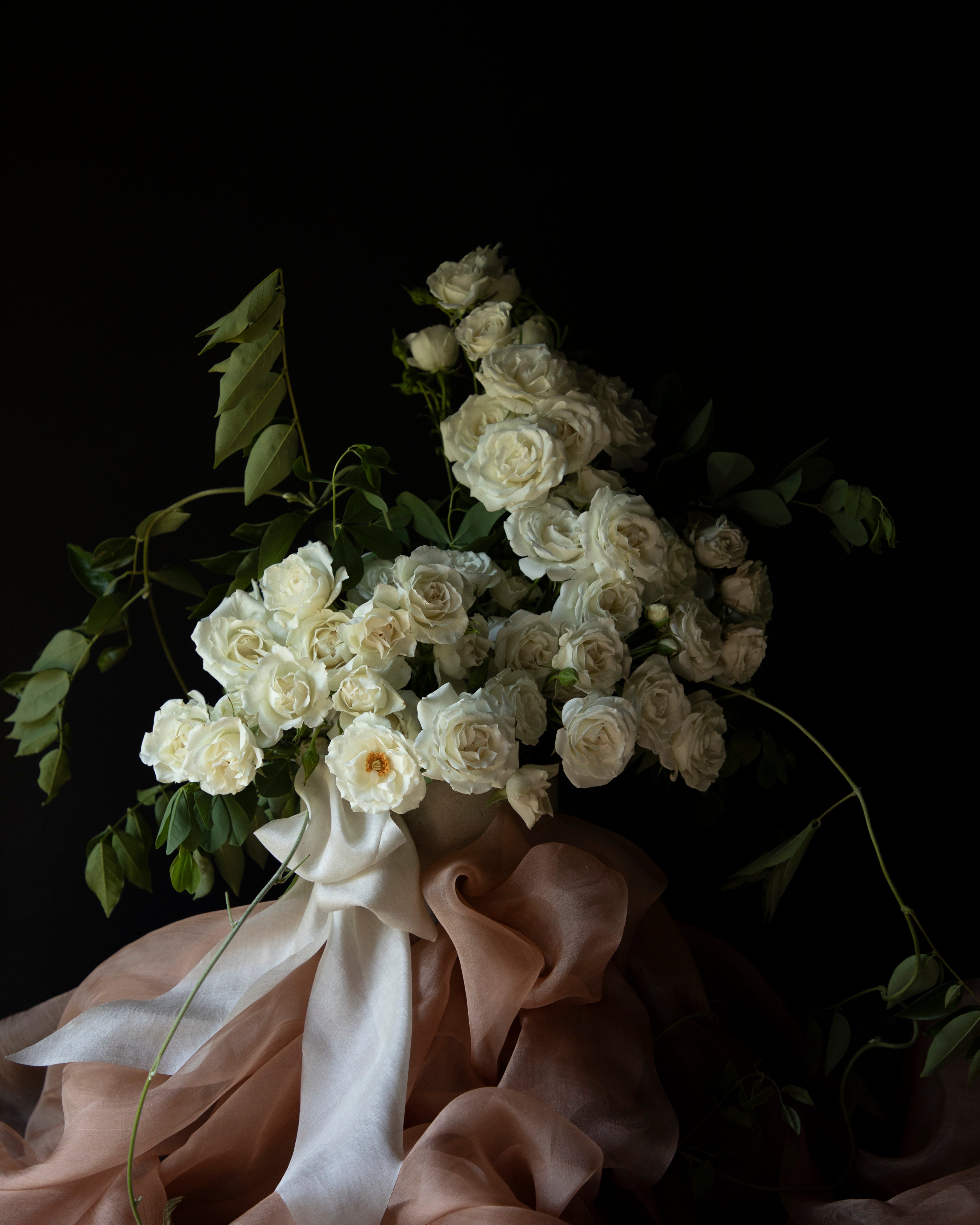 white roses in a floral centerpiece with silk tabletop textiles and ribbons as decor