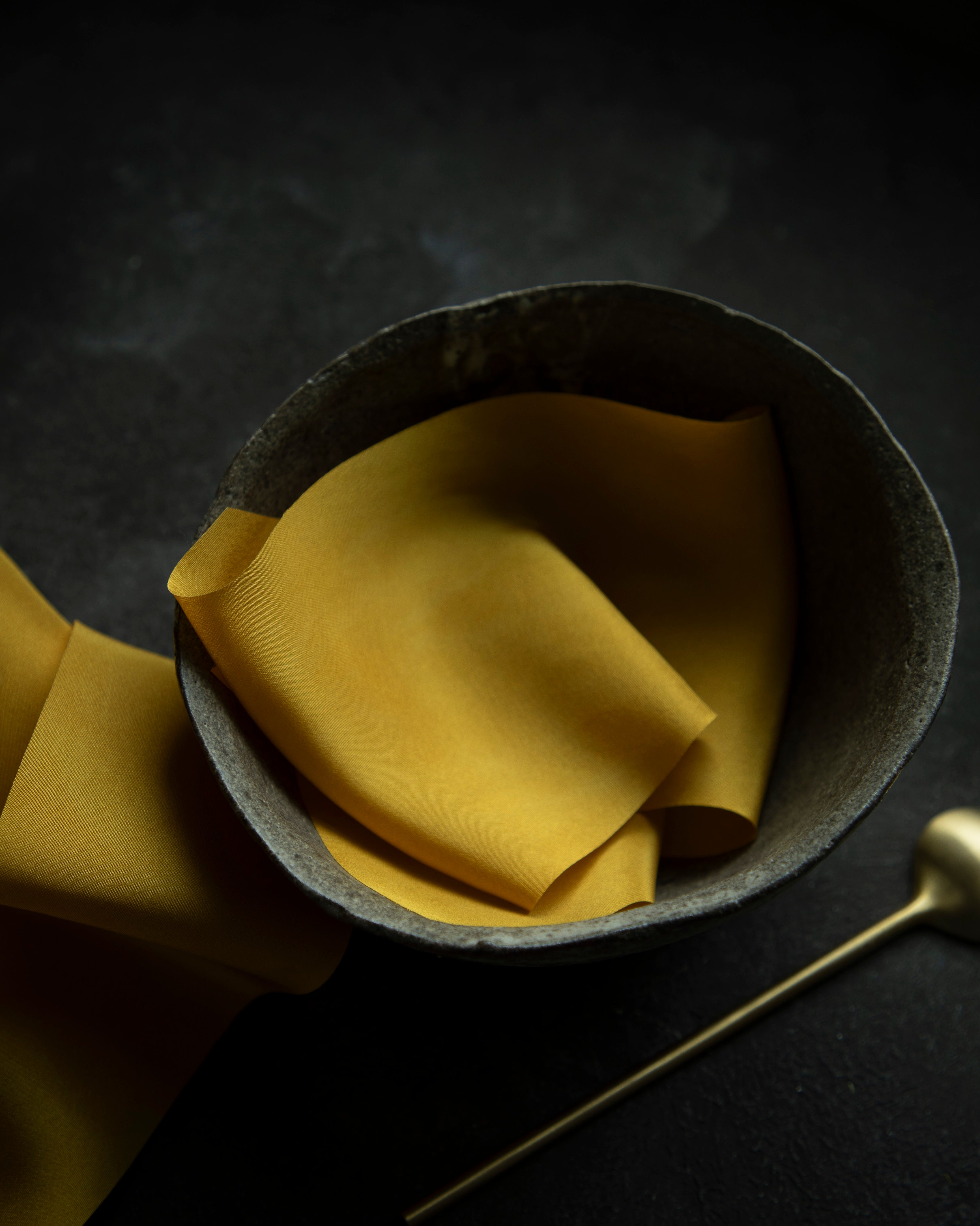 A luxurious plant-dyed silk ribbon in a rich gold hue, elegantly draped, showcasing its soft texture and delicate sheen. Displayed in a ceramic bowl. Ideal for wrapping bridal bouquets, this ribbon is perfect for brides-to-be, engaged couples, and florists looking to add a touch of sophistication to wedding arrangements.