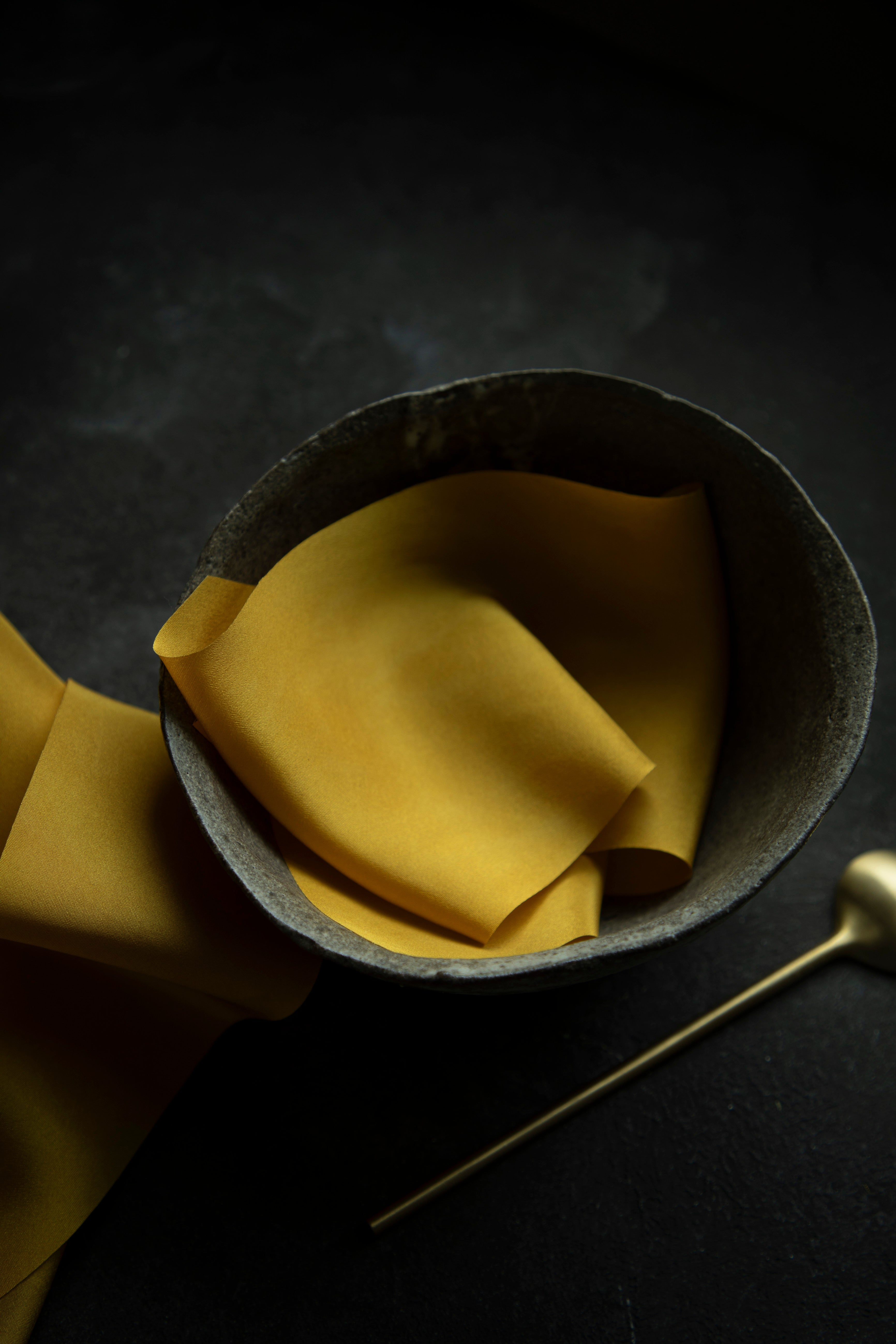 A luxurious plant-dyed silk ribbon in a rich gold hue, elegantly draped, showcasing its soft texture and delicate sheen. Displayed in a ceramic bowl.  Ideal for wrapping bridal bouquets, this ribbon is perfect for brides-to-be, engaged couples, and florists looking to add a touch of sophistication to wedding arrangements.