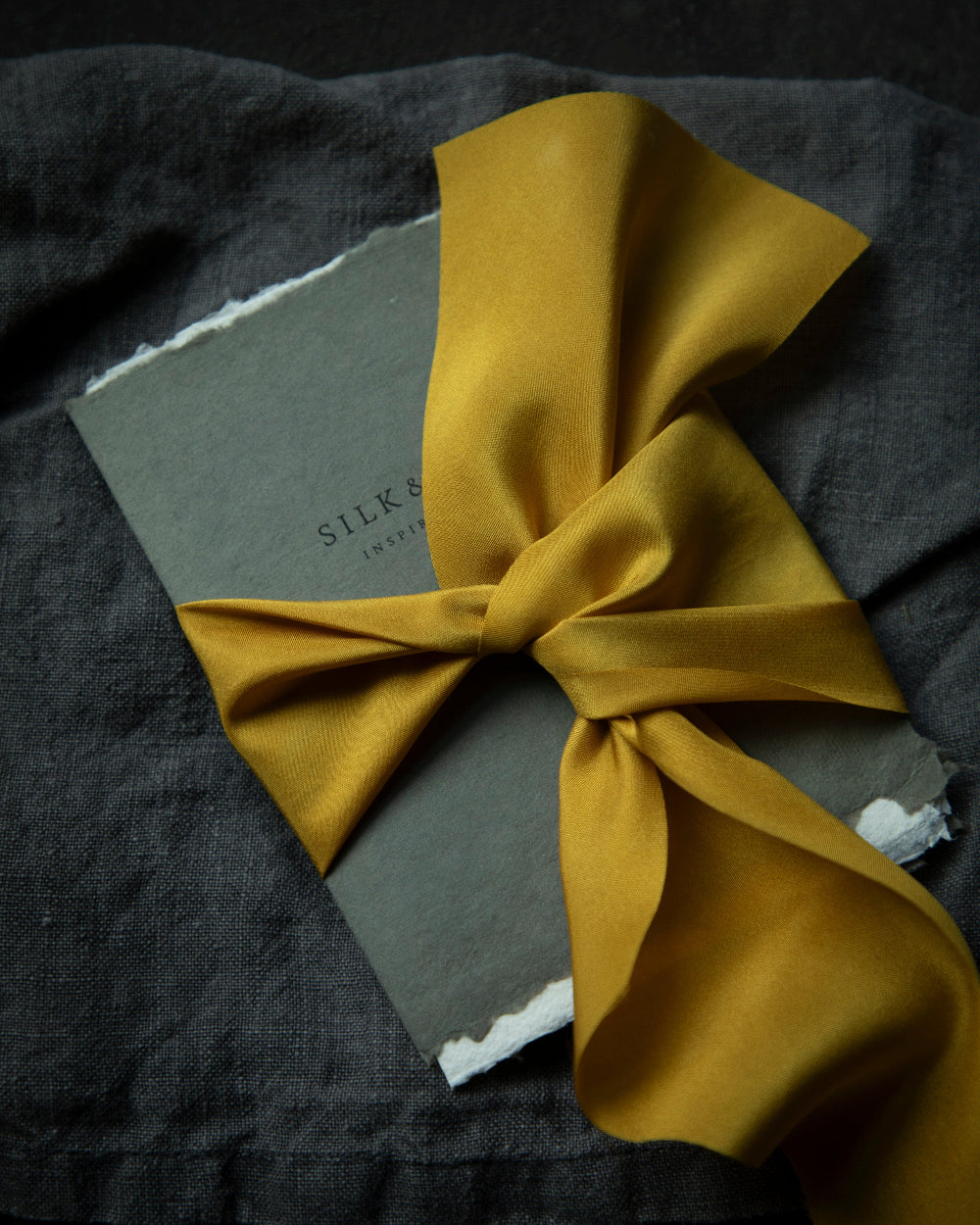 A luxurious plant-dyed silk ribbon in a rich gold hue, elegantly draped, showcasing its soft texture and delicate sheen. Ideal for wrapping bridal bouquets, and wedding invitations, this ribbon is perfect for brides-to-be, engaged couples, and florists looking to add a touch of sophistication to wedding arrangements.
