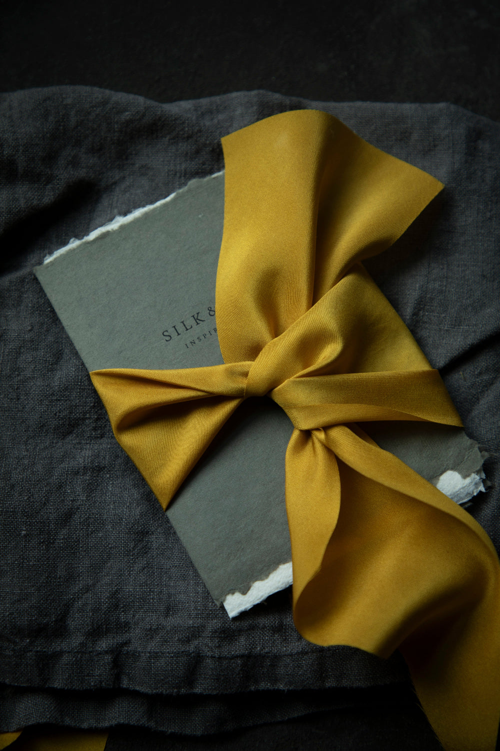 A luxurious plant-dyed silk ribbon in a rich gold hue, elegantly draped, showcasing its soft texture and delicate sheen. Ideal for wrapping bridal bouquets, and wedding invitations, this ribbon is perfect for brides-to-be, engaged couples, and florists looking to add a touch of sophistication to wedding arrangements.