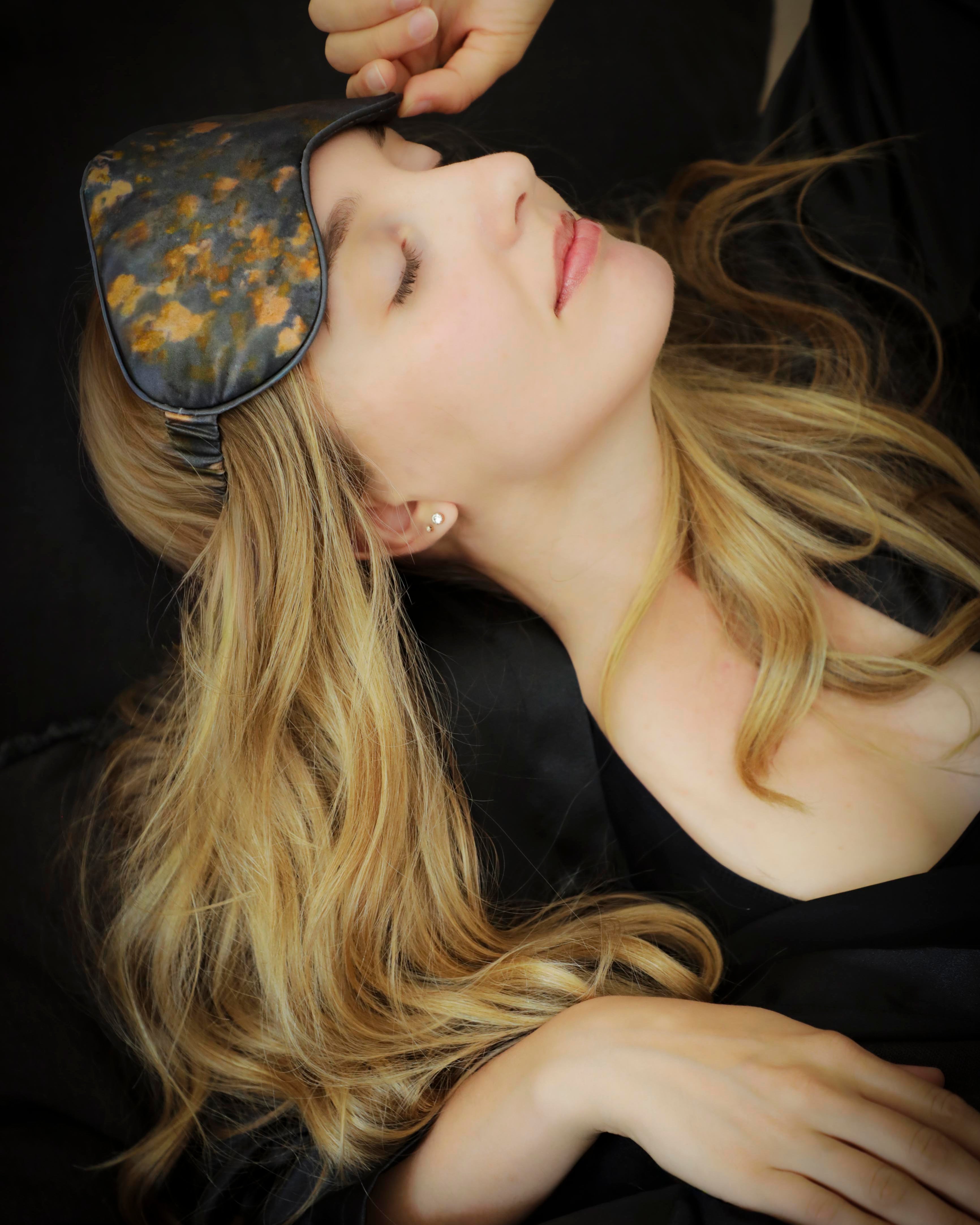 Woman wearing a floral silk sleep mask with a dark, moody background