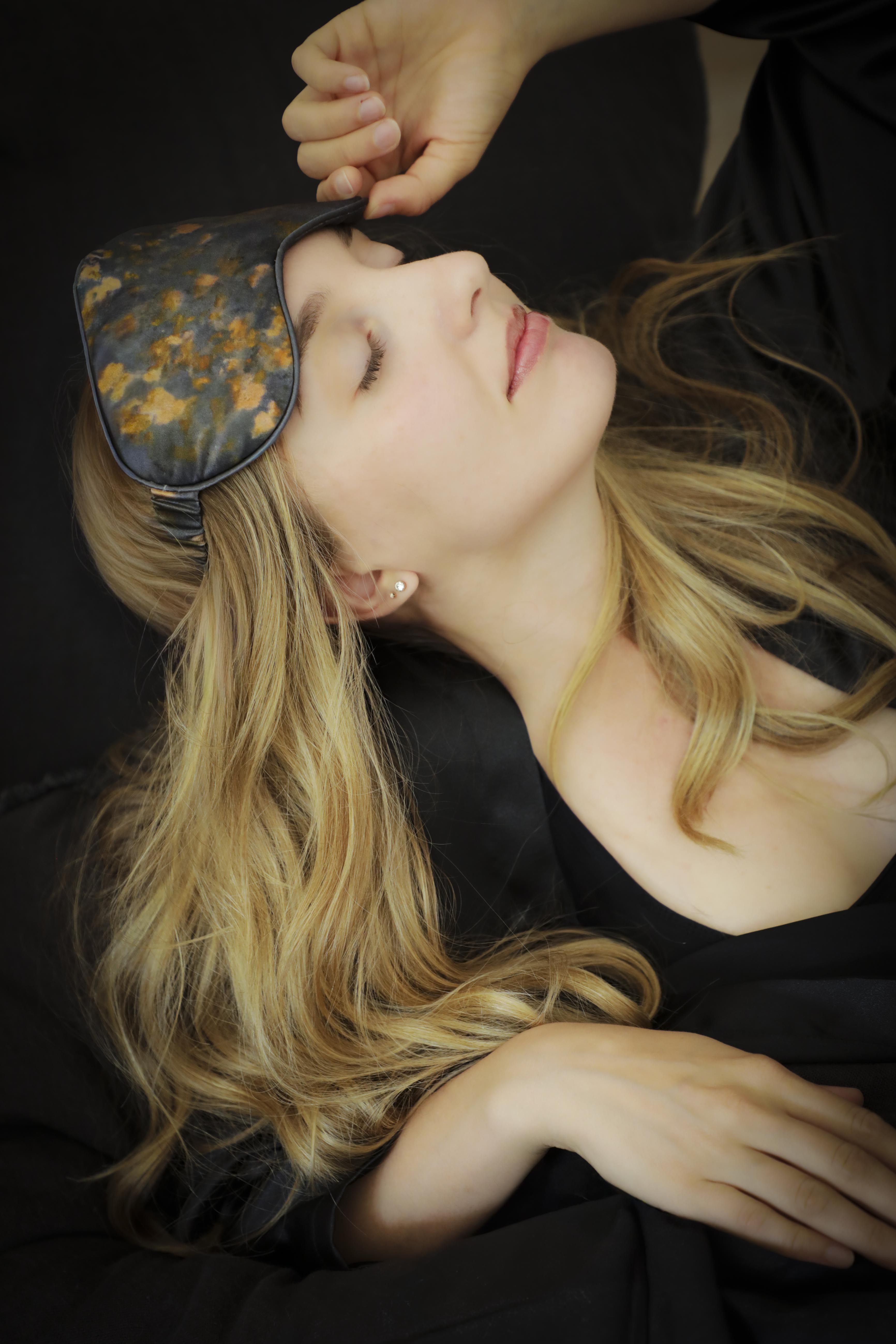 Woman wearing a floral silk sleep mask with a dark, moody background