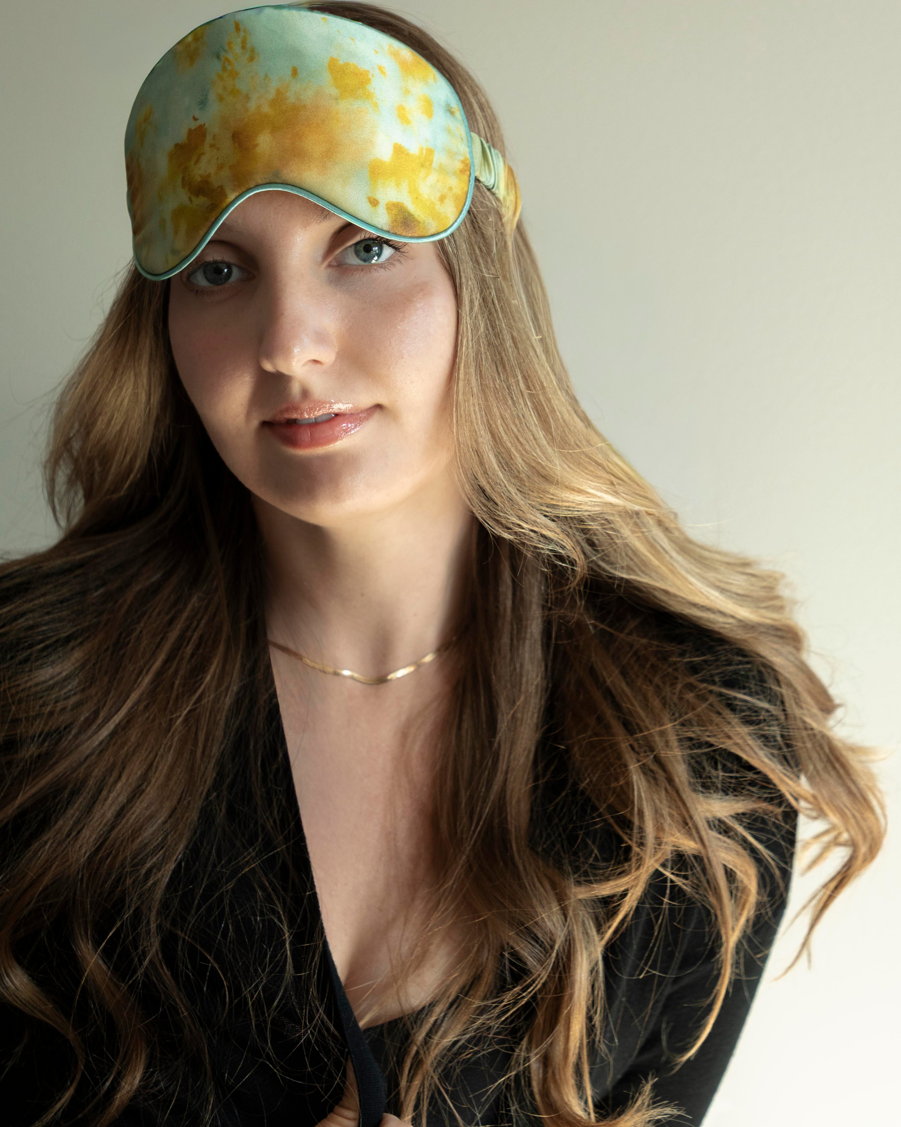 Woman wearing a yellow and green patterned sleep mask against a neutral background