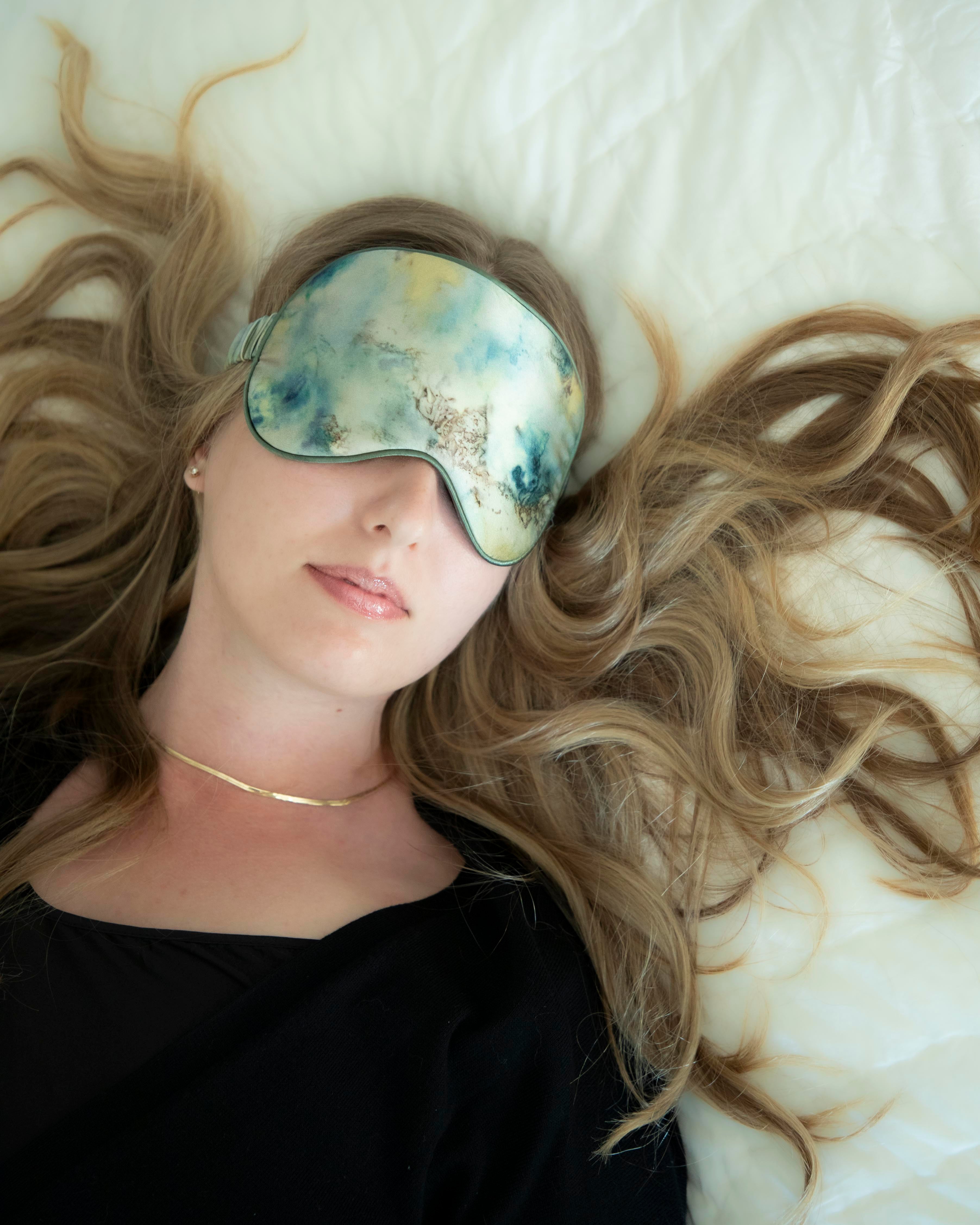 Woman wearing a botanical print silk sleep eye mask as featured on with long blonde hair on a white background