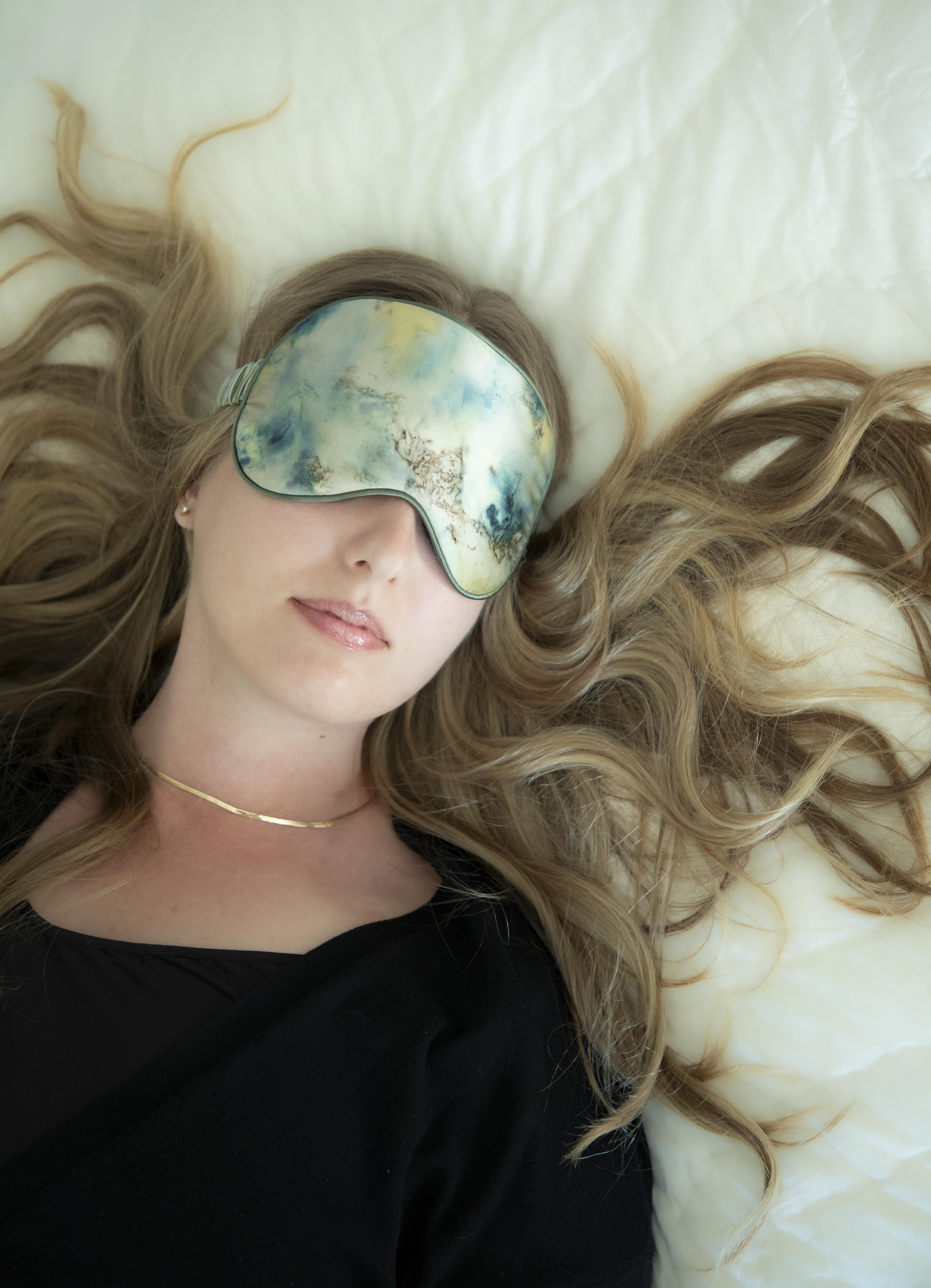 Woman wearing a botanical print silk sleep eye mask as featured on with long blonde hair on a white background