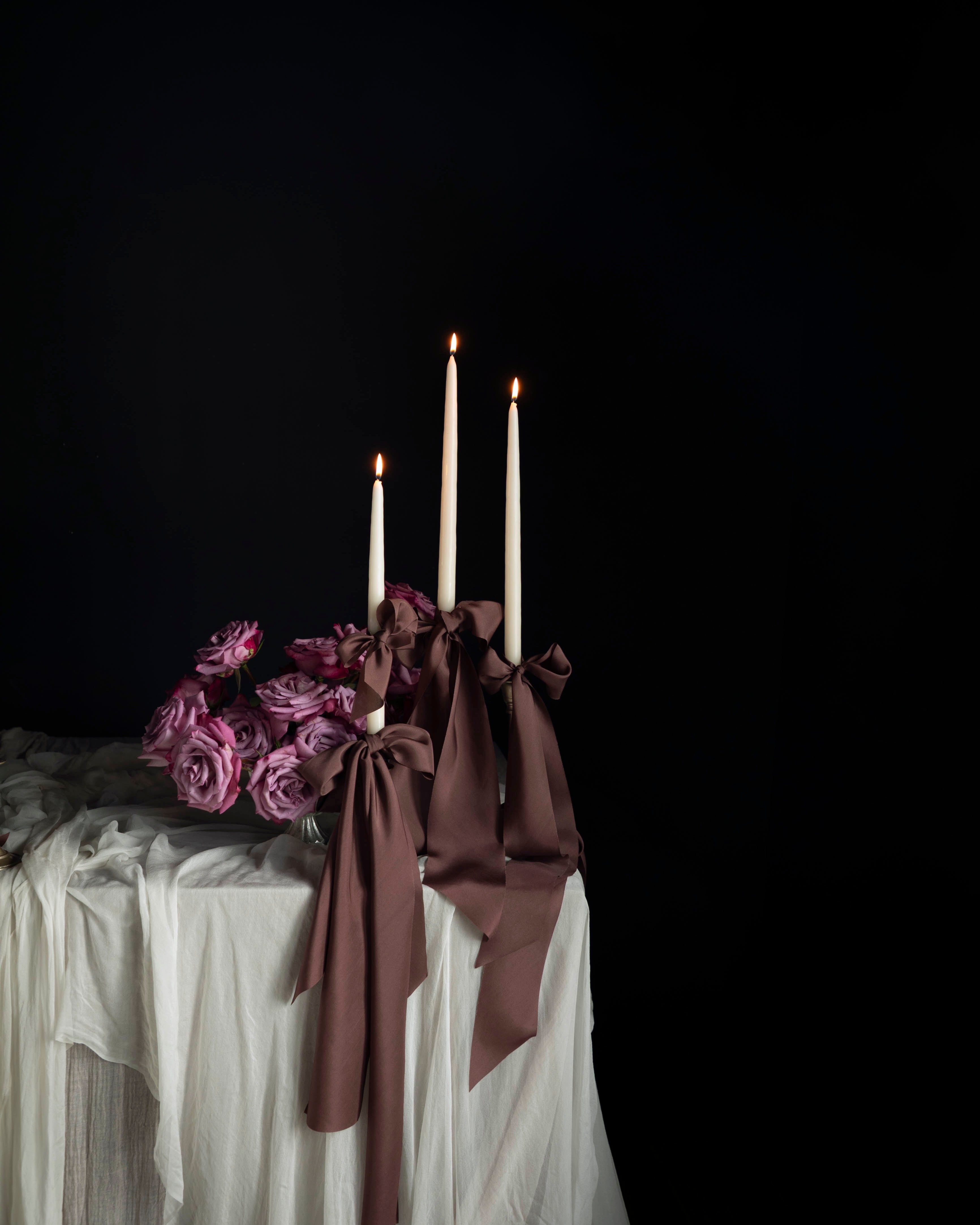 Decorative table setting with candles and flowers against a dark background. Featuring Silk & Willow Chocolate Rose silk ribbons.