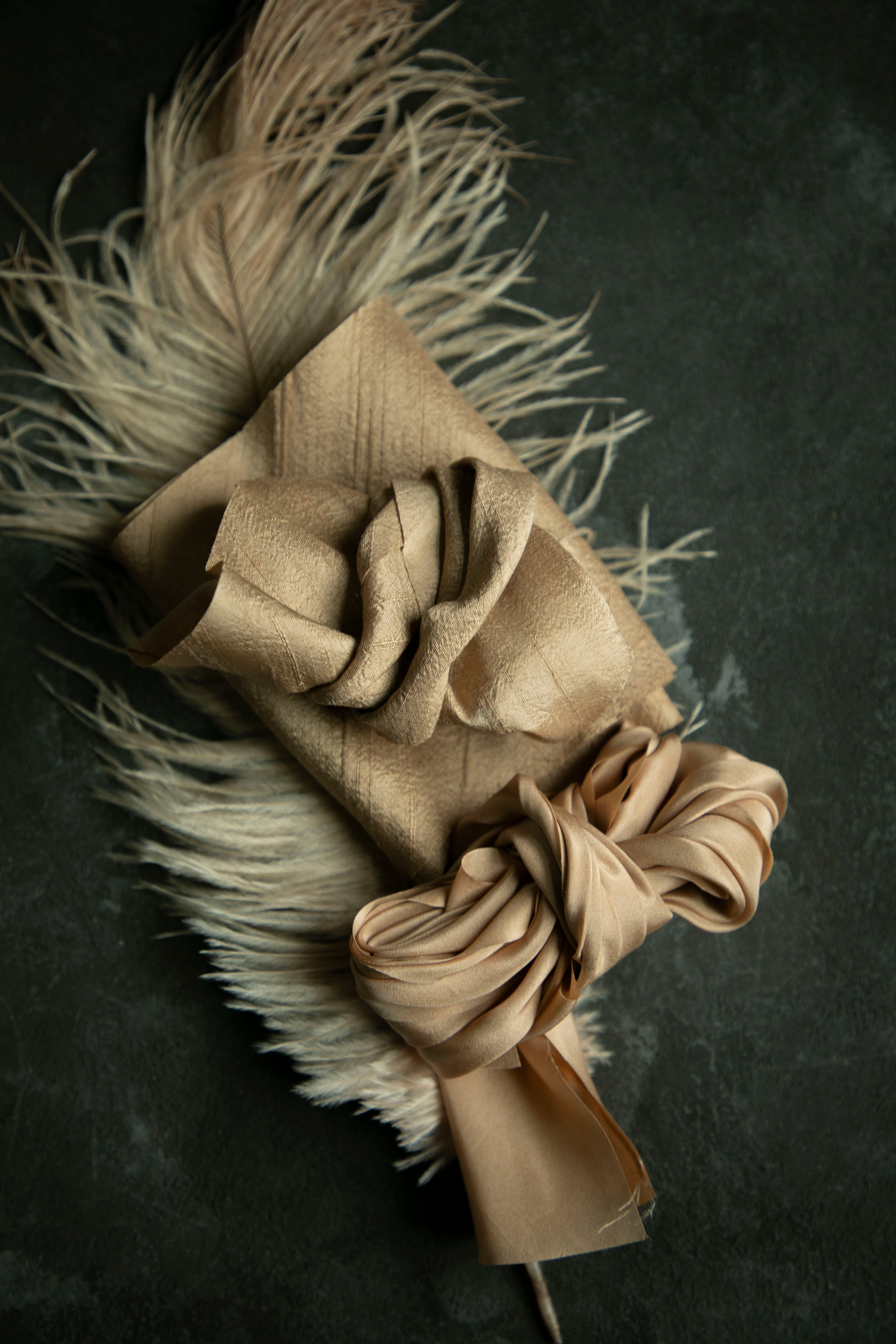 A hand-loomed cinnamon dupioni silk ribbon with a matte textured finish, displayed on a dark background with a feather accessory.