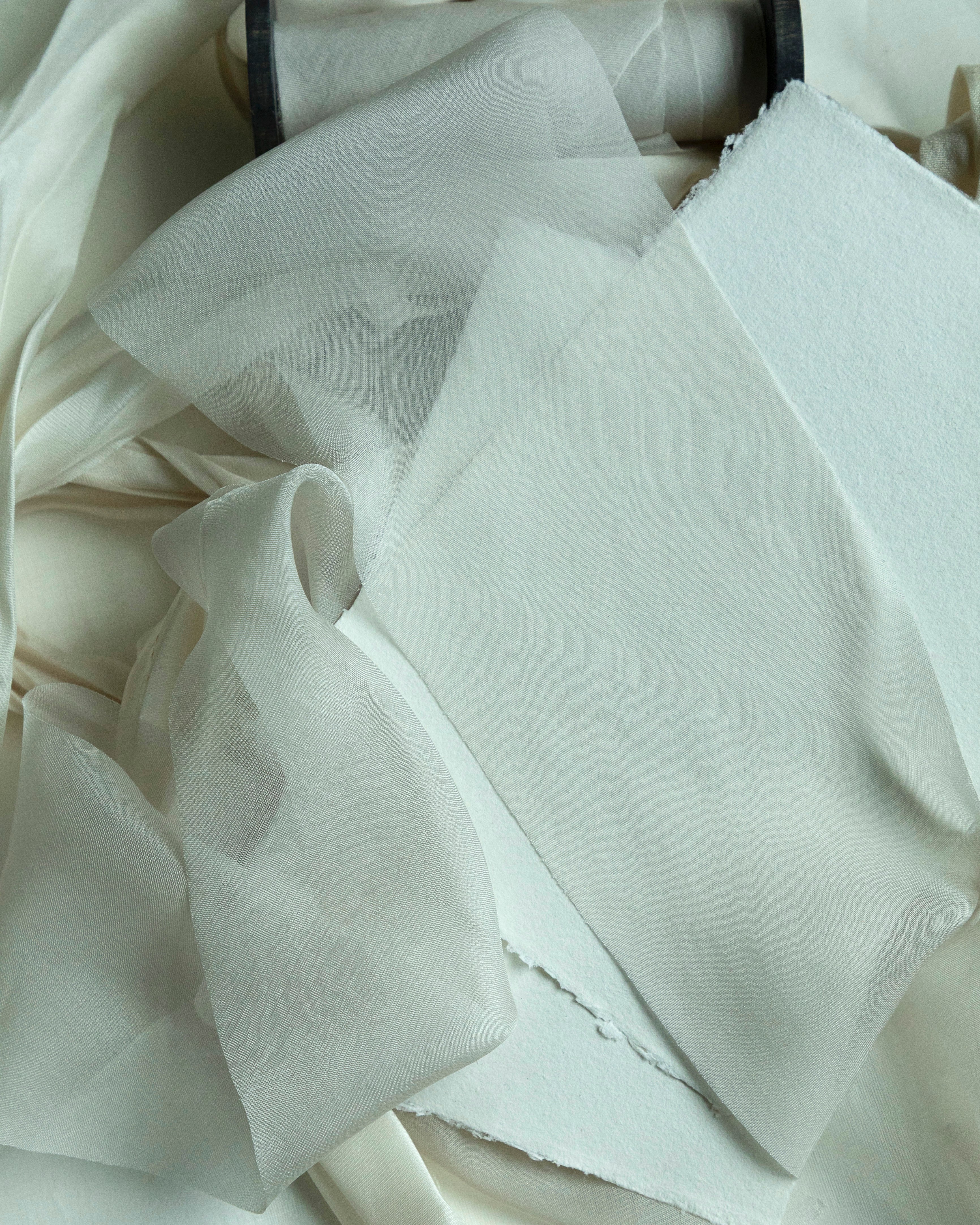 Close-up of dove silk ribbon on a wooden spool, ribbon is draped around handmade paper on a light background