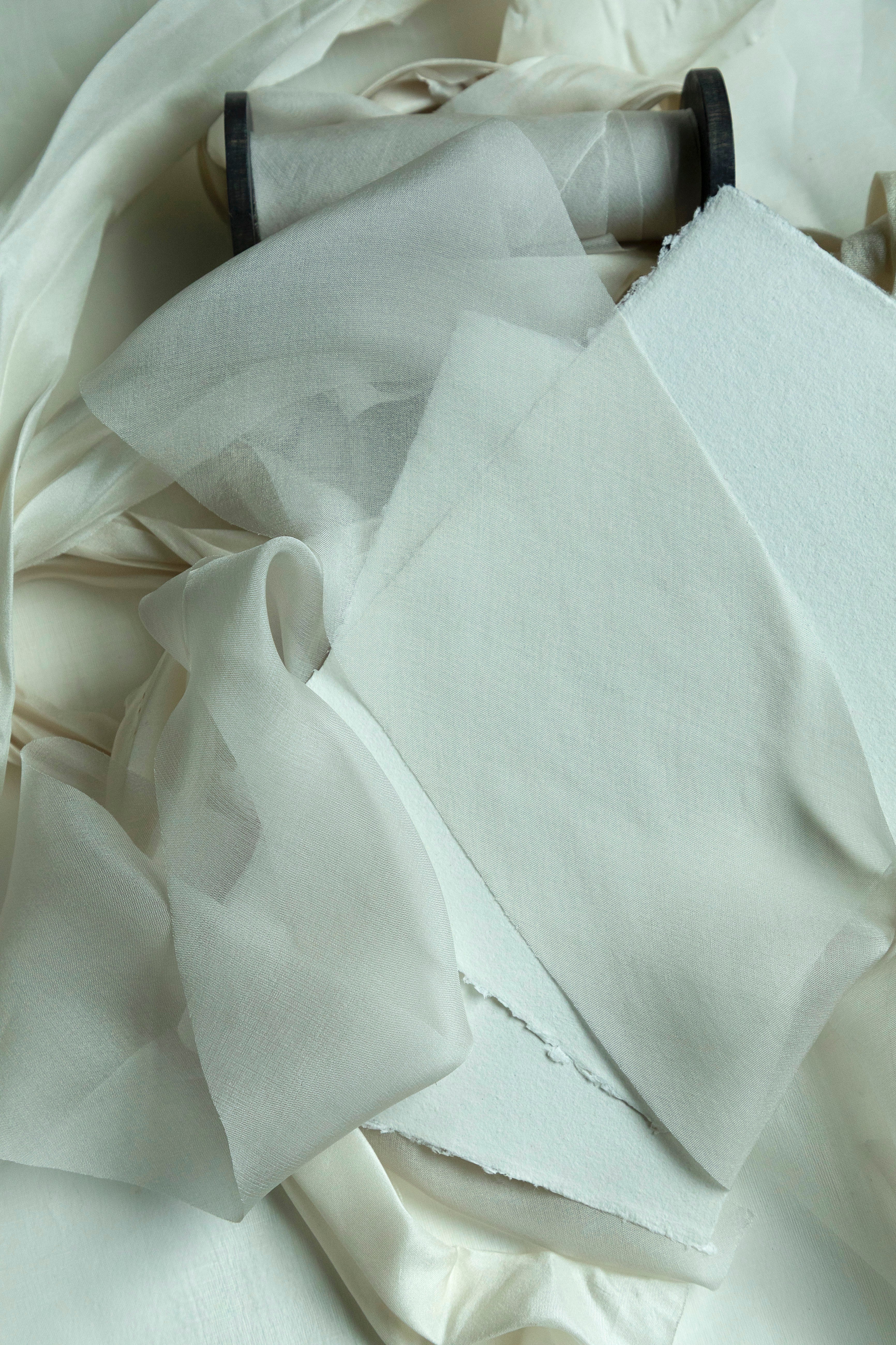 Close-up of dove silk ribbon on a wooden spool, ribbon is draped around handmade paper on a light background