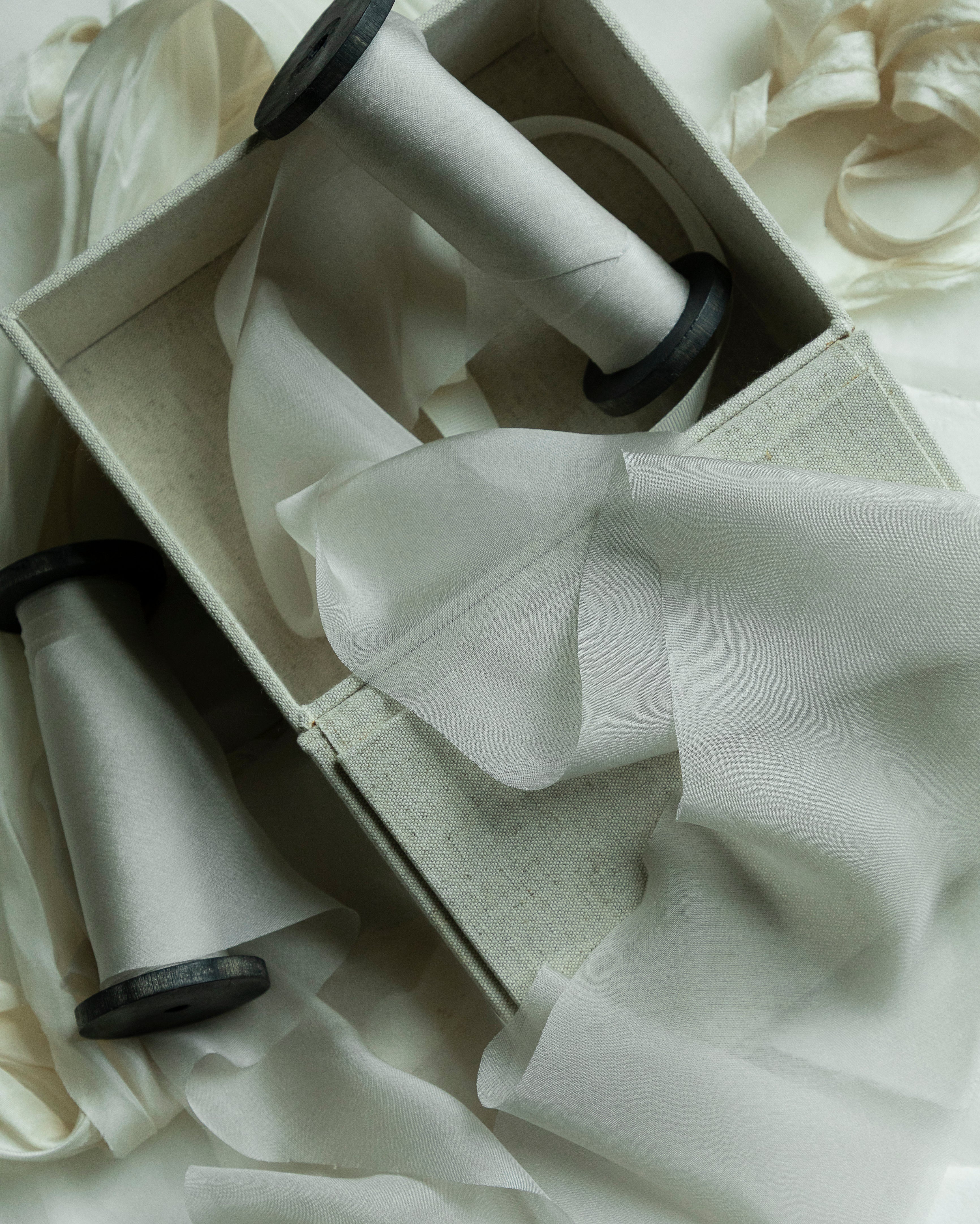 A box with spools of light gray ribbons and soft, sheer fabric draped around it
