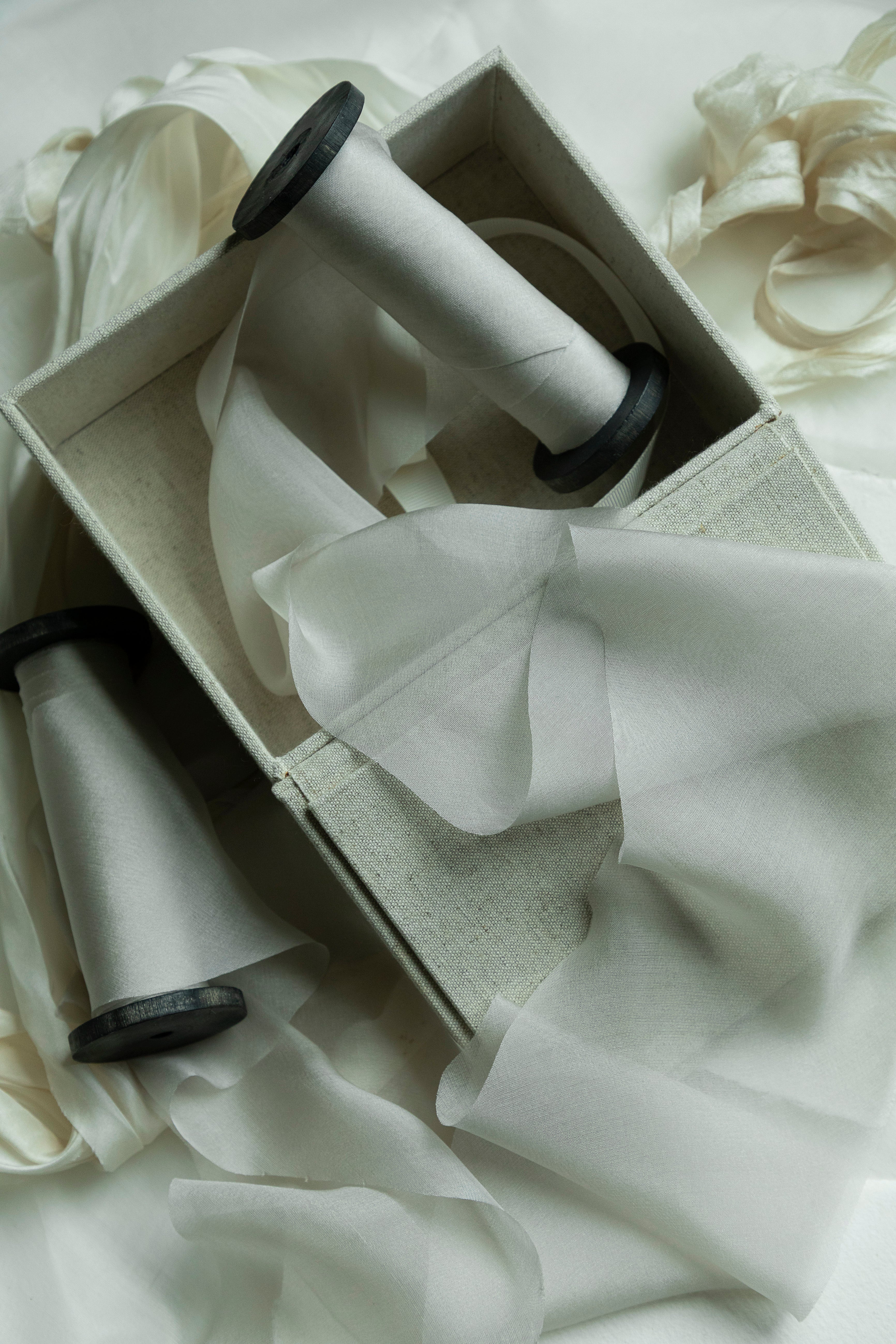 A box with spools of light gray ribbons and soft, sheer fabric draped around it