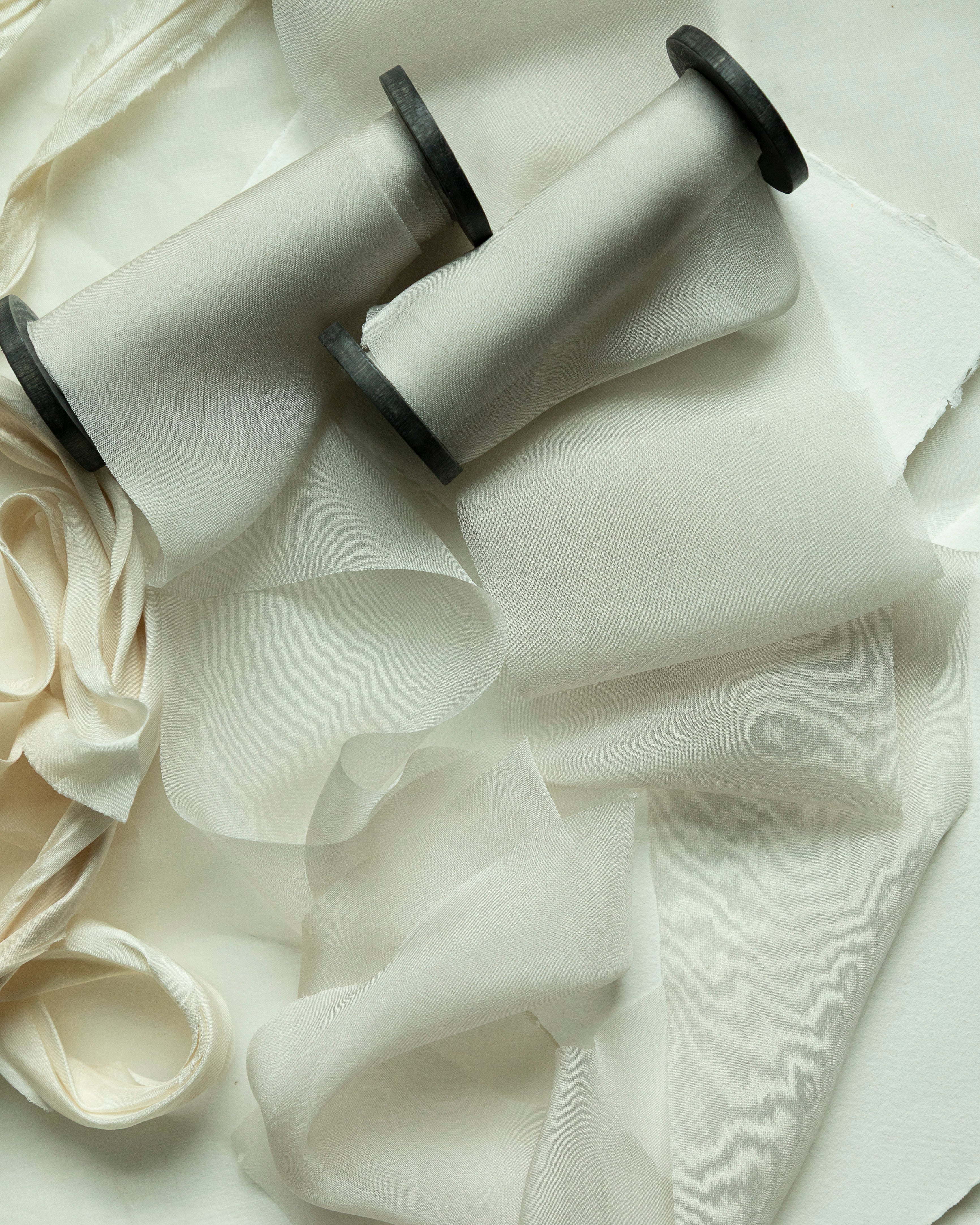 Two spools of white ribbons on a textured white fabric background