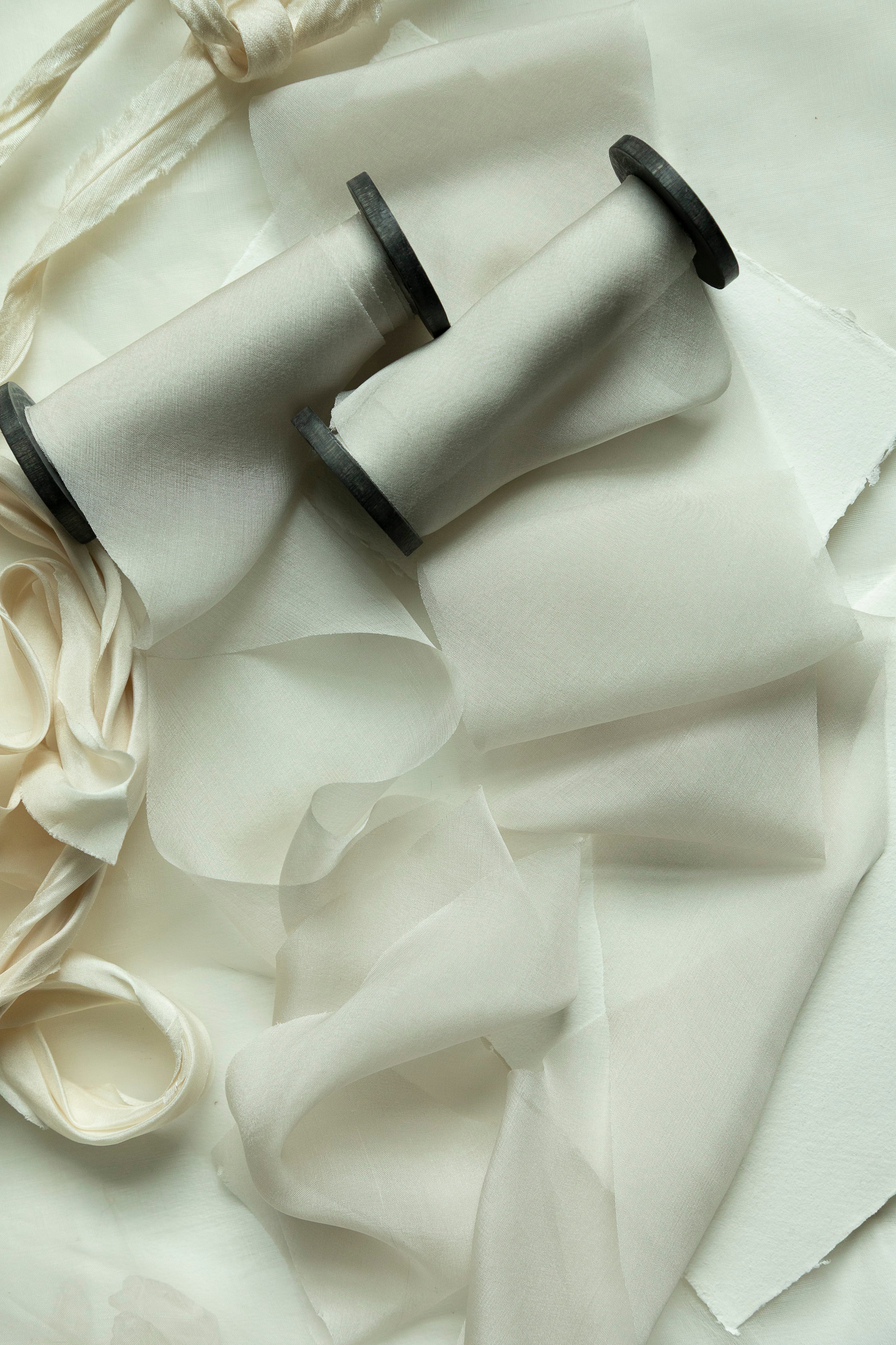 Two spools of white ribbons on a textured white fabric background