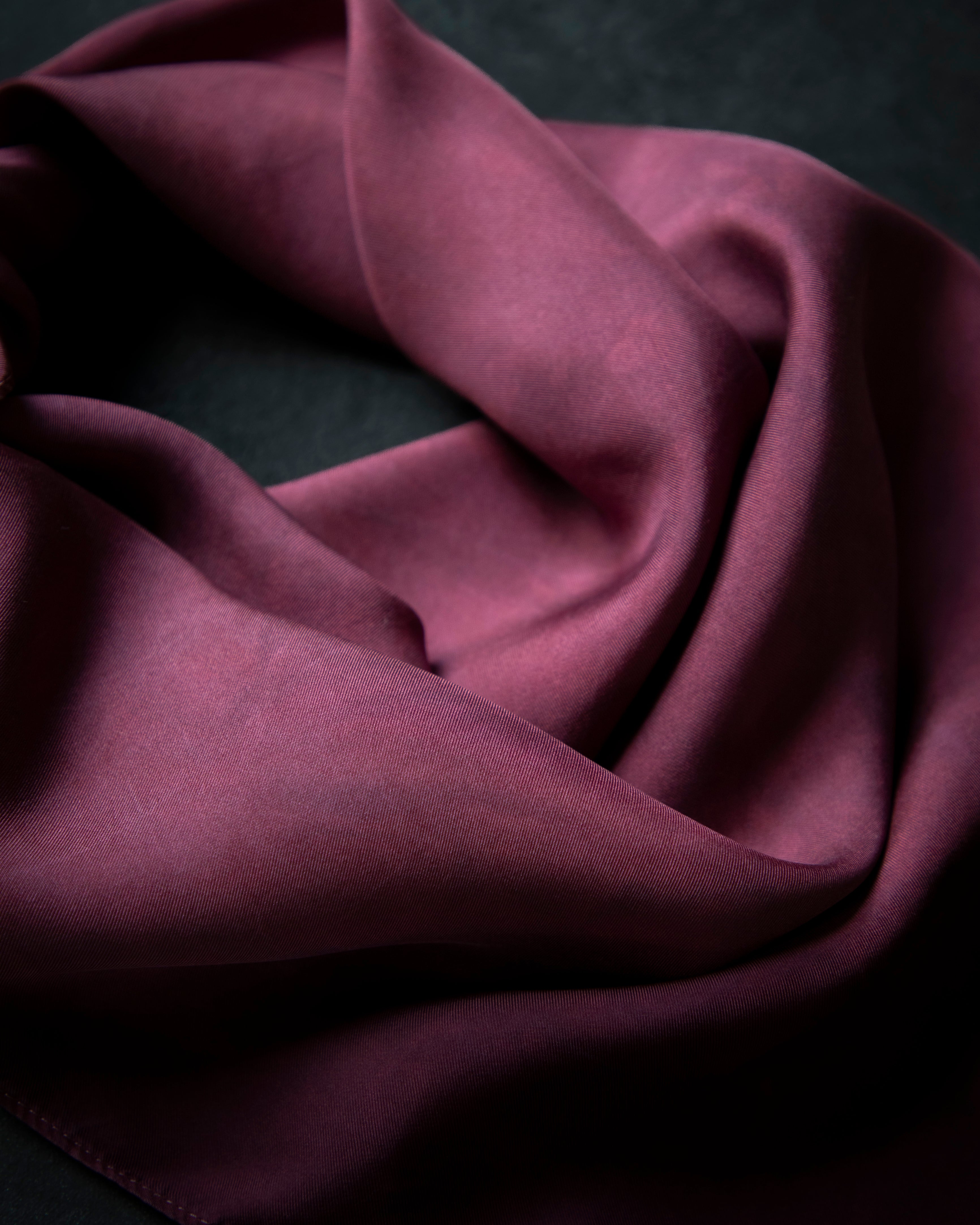 A draped piece of deep burgundy silk fabric with soft folds and a subtle sheen, set against a dark textured background.