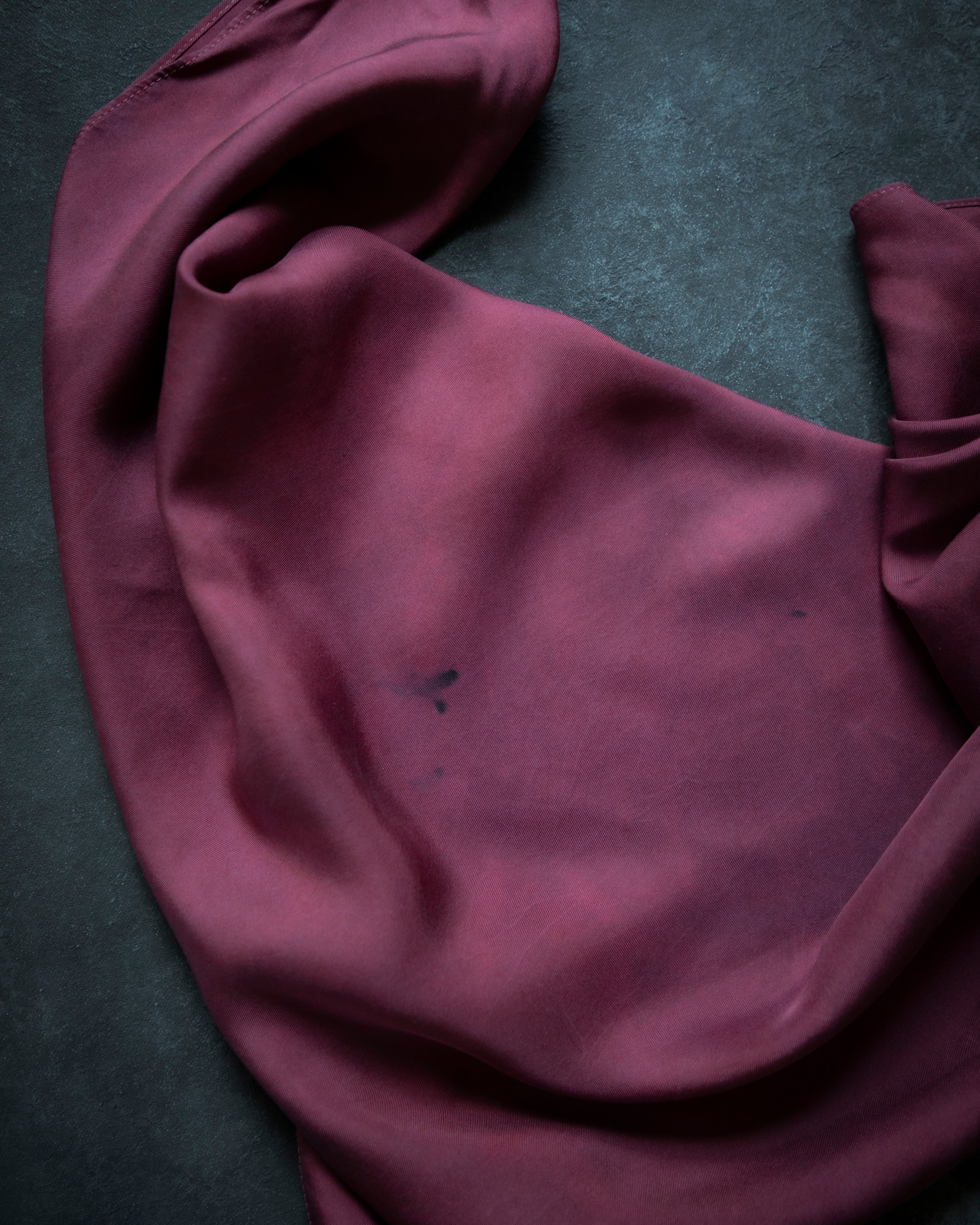 A draped piece of deep plum purple fabric, likely silk or satin, laid out on a dark textured gray surface.
