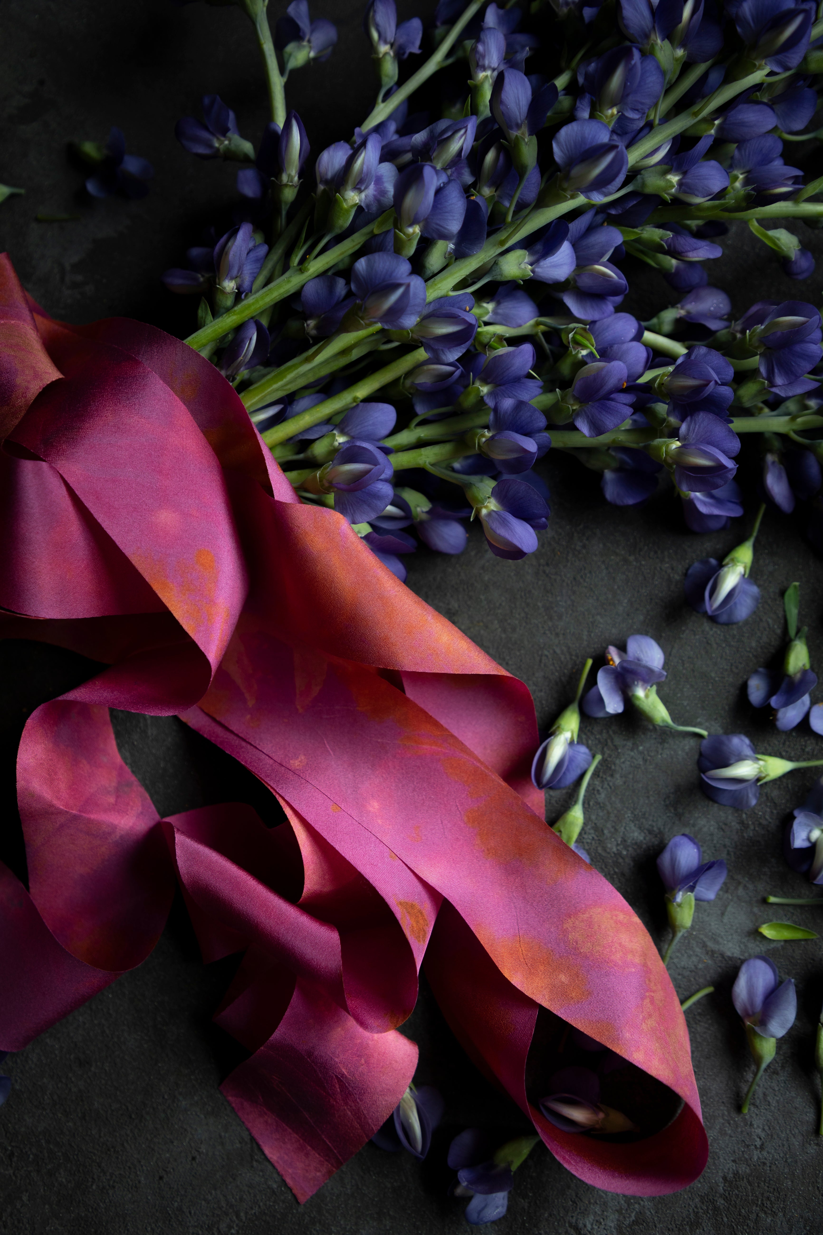 Purple flowers with a pink ribbon on a dark surface