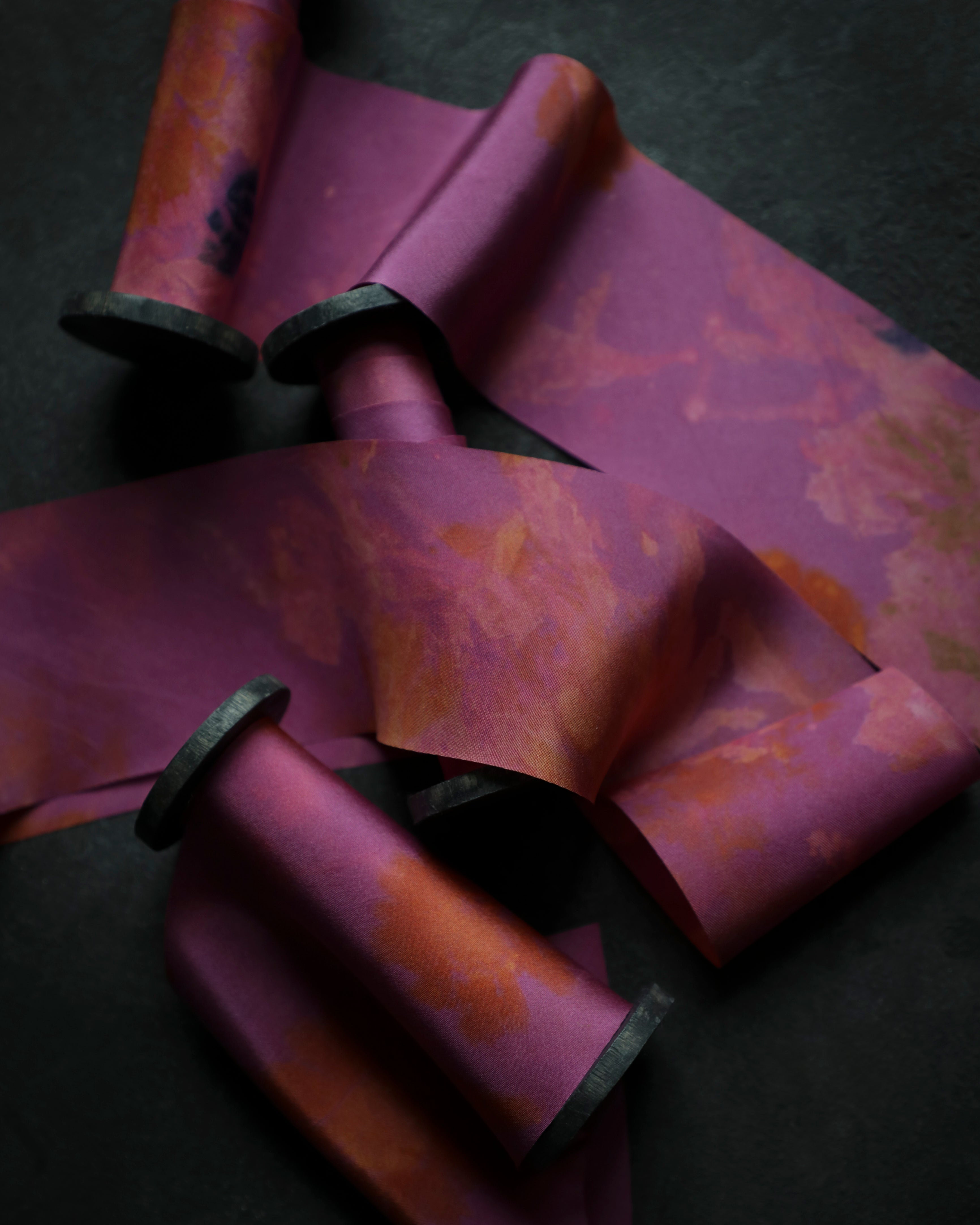 hot pink silk ribbons on black wooden spools on a dark surface