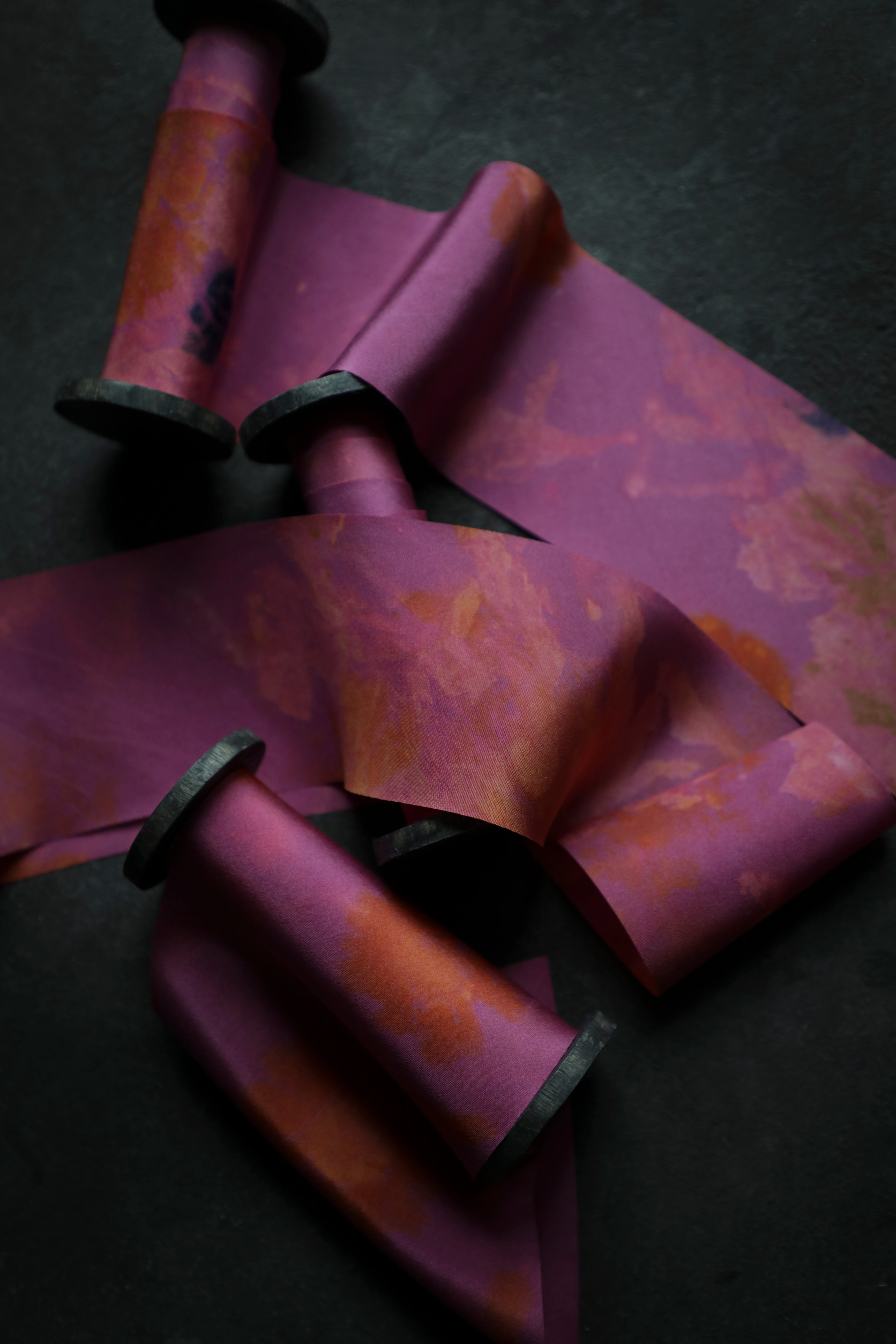 hot pink silk ribbons on black wooden spools on a dark surface