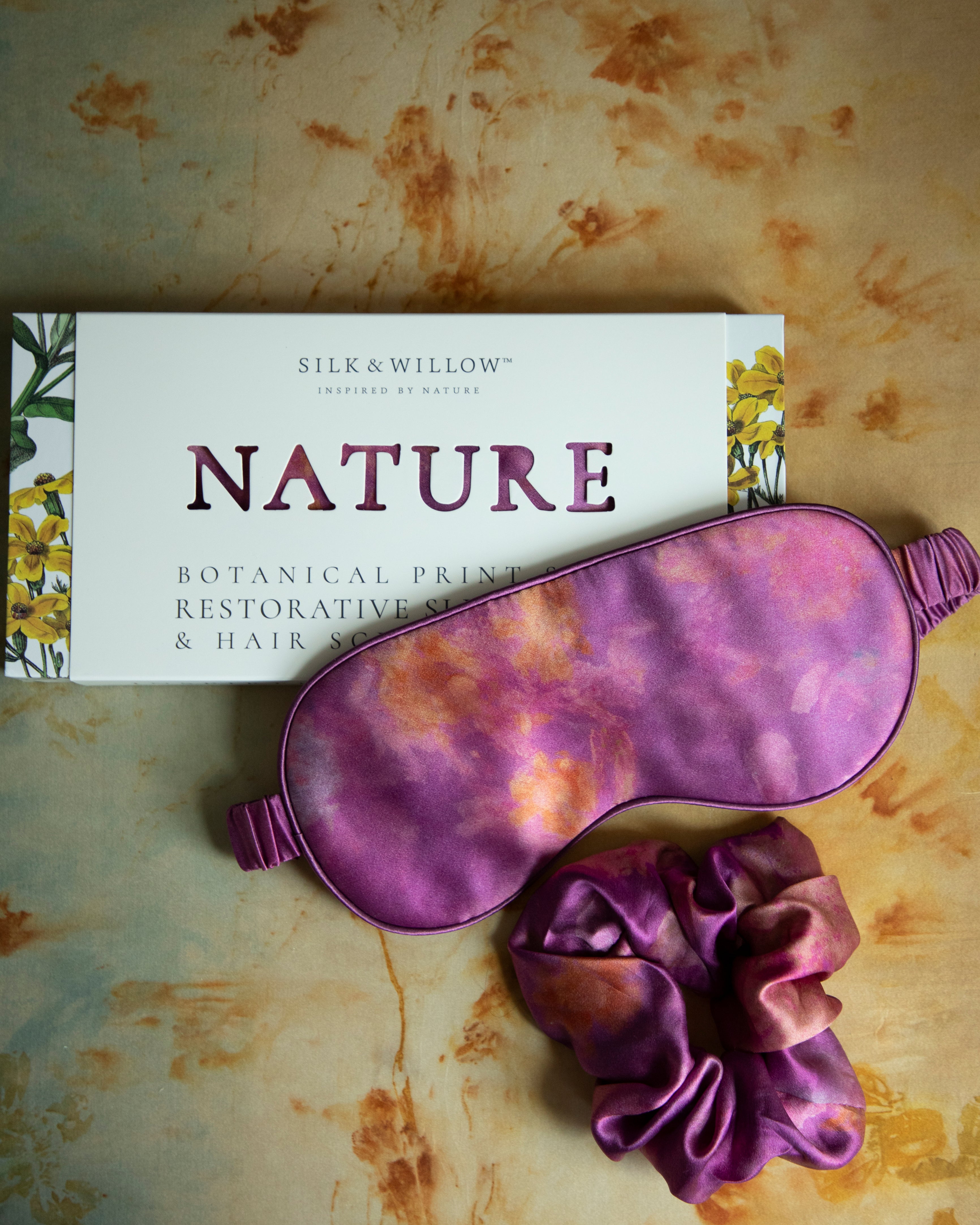 A luxurious silk sleep mask and hair scrunchie set featuring delicate botanical patterns, elegantly displayed in a sustainable gift box, perfect for a sophisticated and eco-conscious touch.
