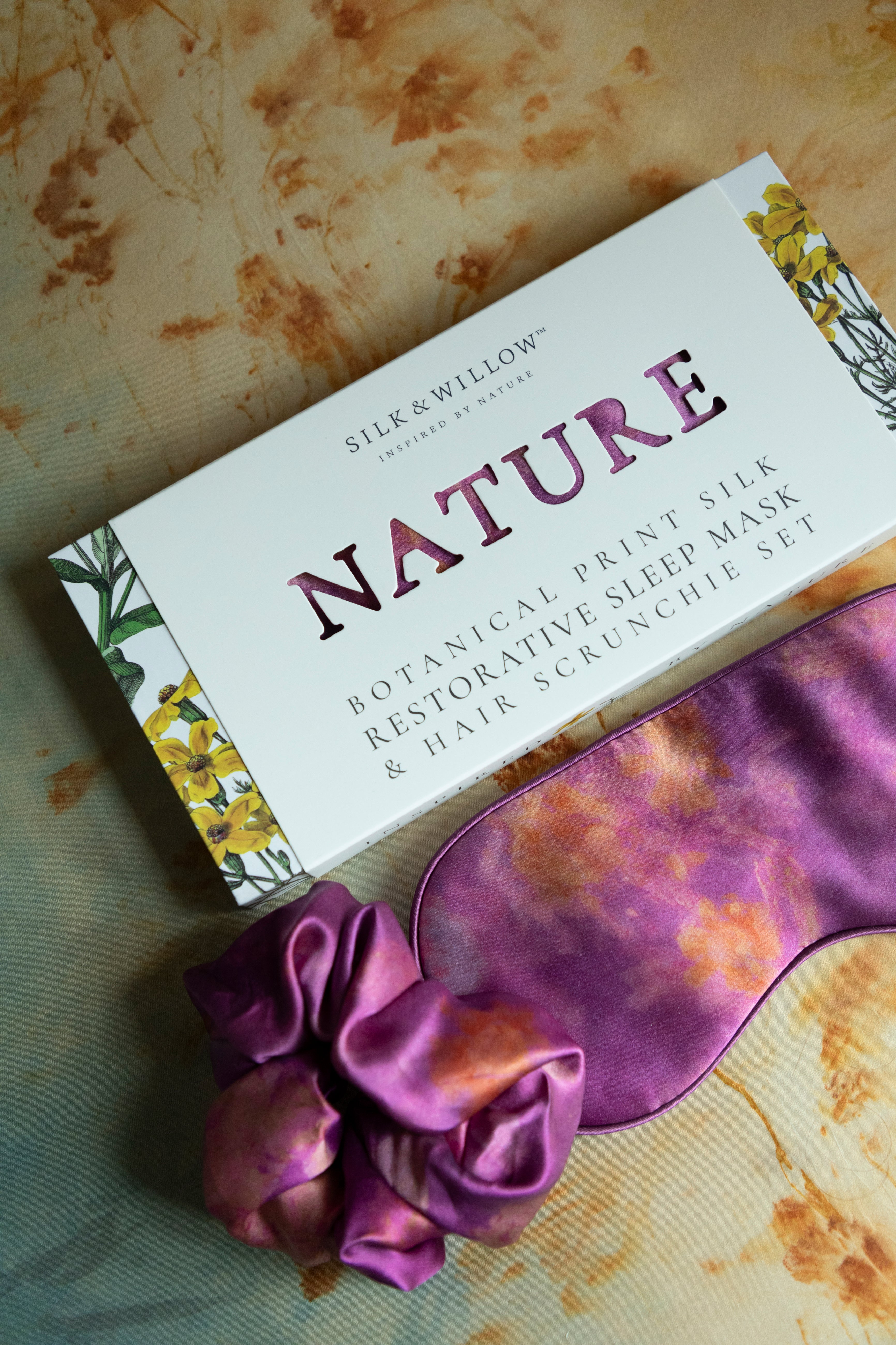 A luxurious silk sleep mask and hair scrunchie set featuring delicate botanical patterns, elegantly displayed in a sustainable gift box, perfect for a sophisticated and eco-conscious touch.