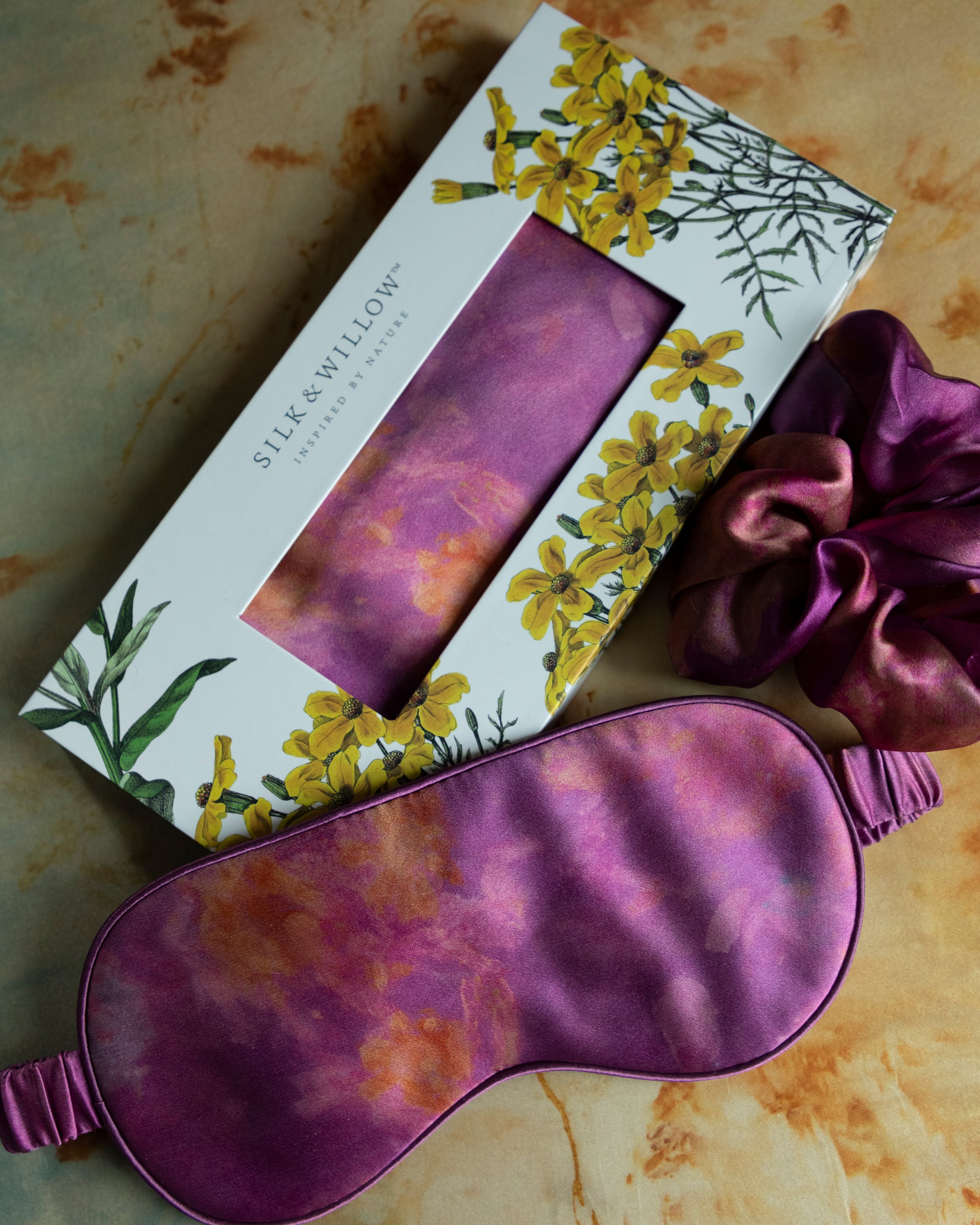 A luxurious silk sleep mask and hair scrunchie set featuring delicate botanical patterns, elegantly displayed in a sustainable gift box, perfect for a sophisticated and eco-conscious touch.