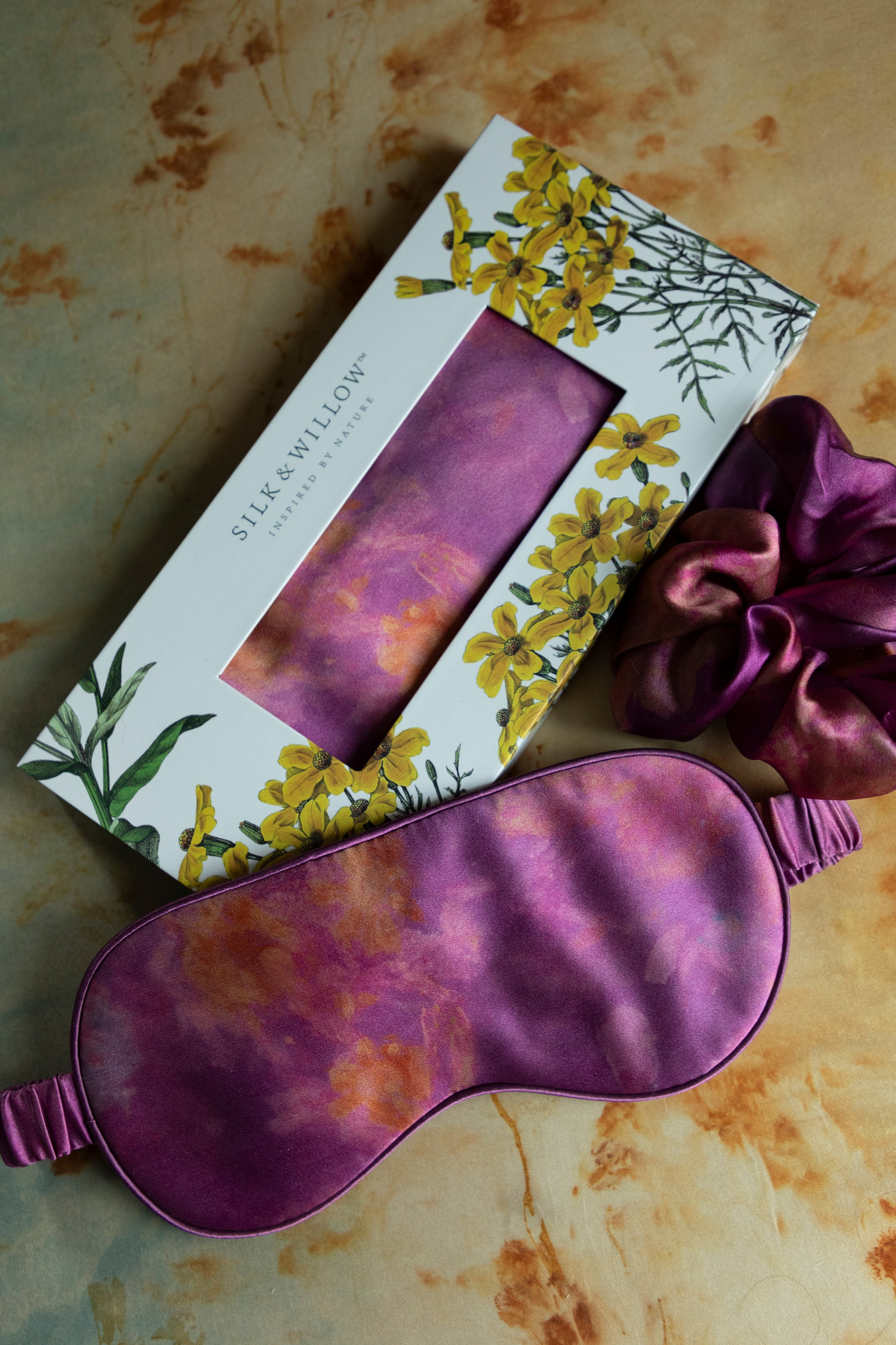 A luxurious silk sleep mask and hair scrunchie set featuring delicate botanical patterns, elegantly displayed in a sustainable gift box, perfect for a sophisticated and eco-conscious touch.