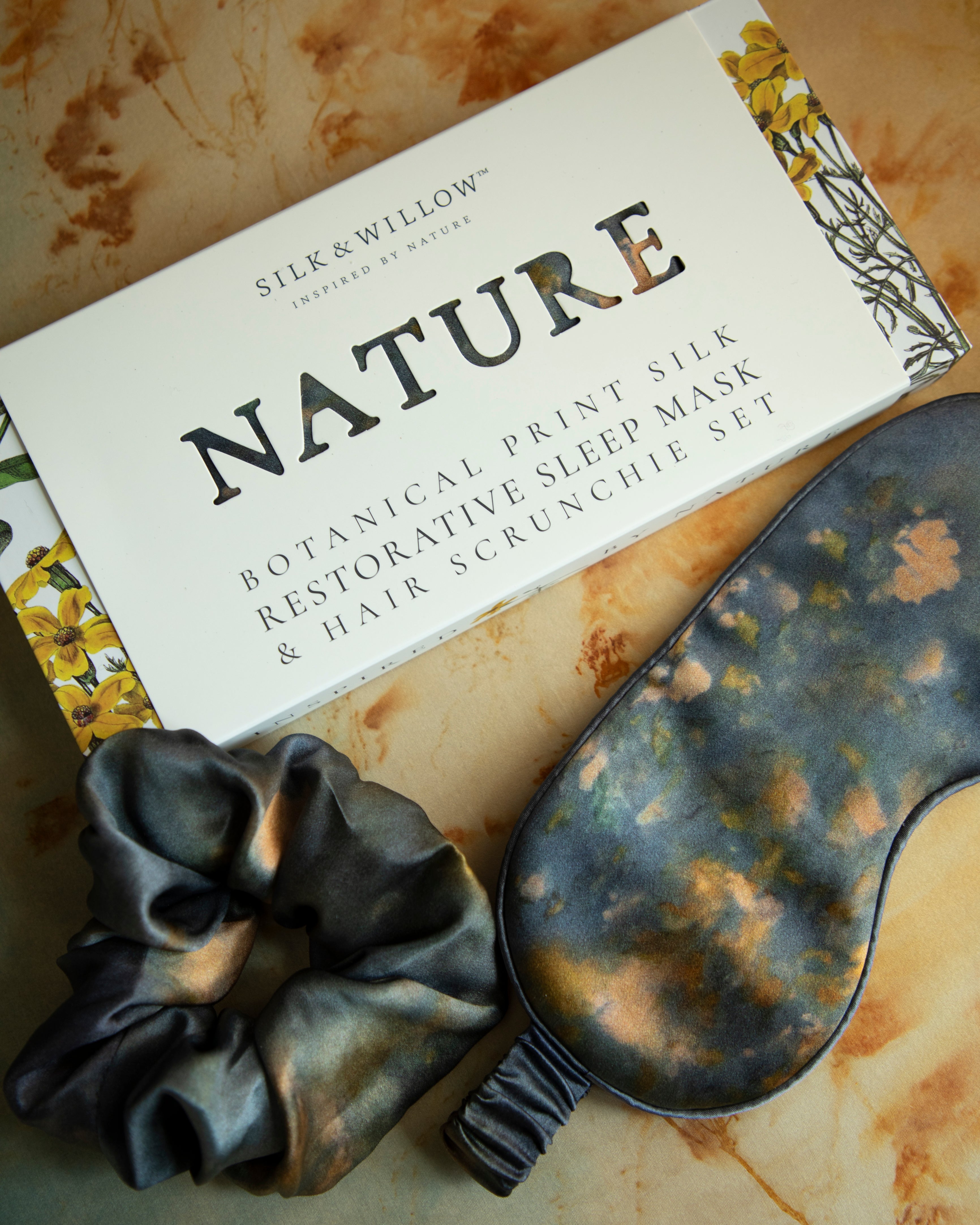 A luxurious silk sleep mask and hair scrunchie set featuring delicate botanical patterns, elegantly displayed in a sustainable gift box, perfect for a sophisticated and eco-conscious touch.