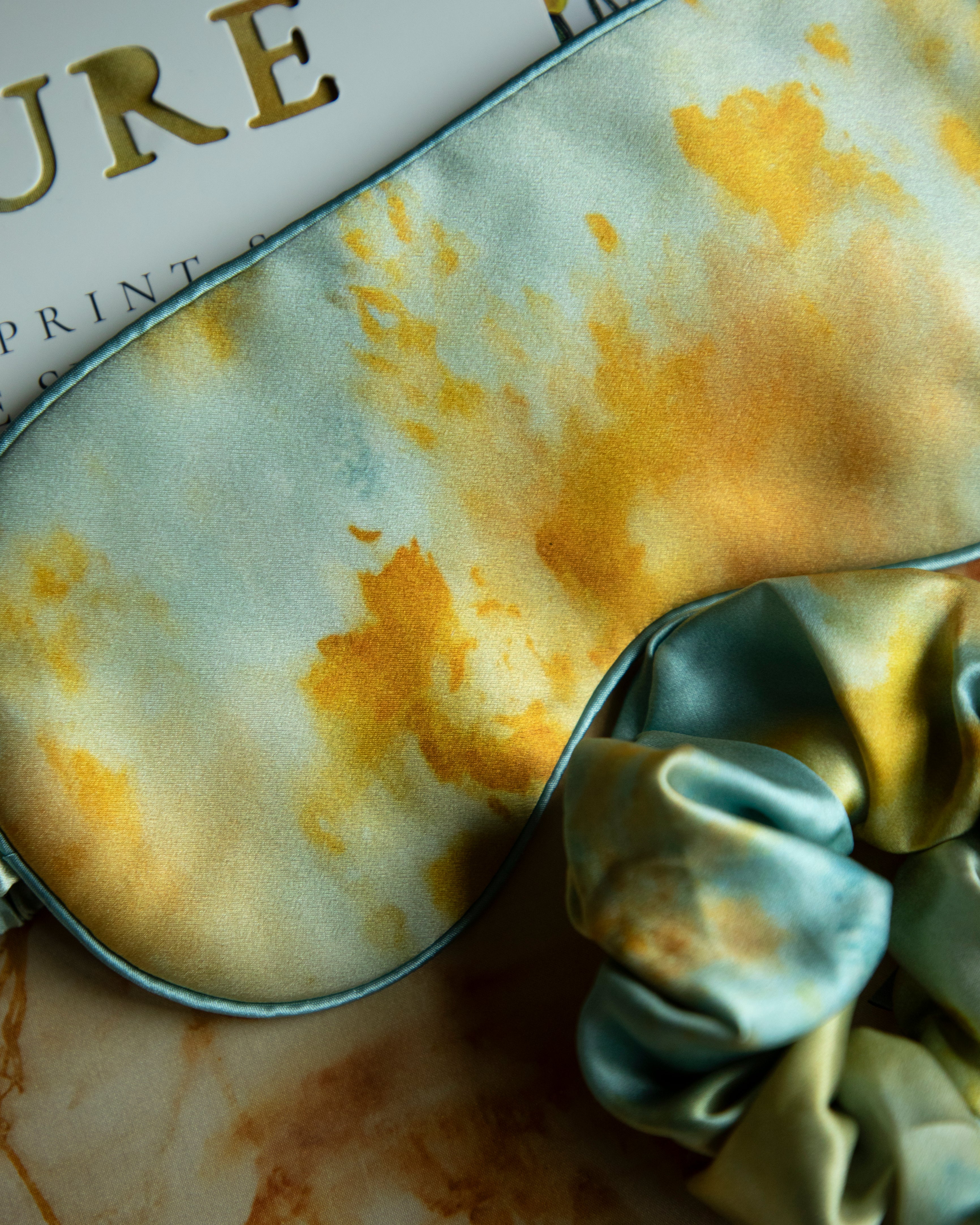 Silk & Willow Nature botanical print silk restorative sleep mask and hair scrunchie set on a textured surface.