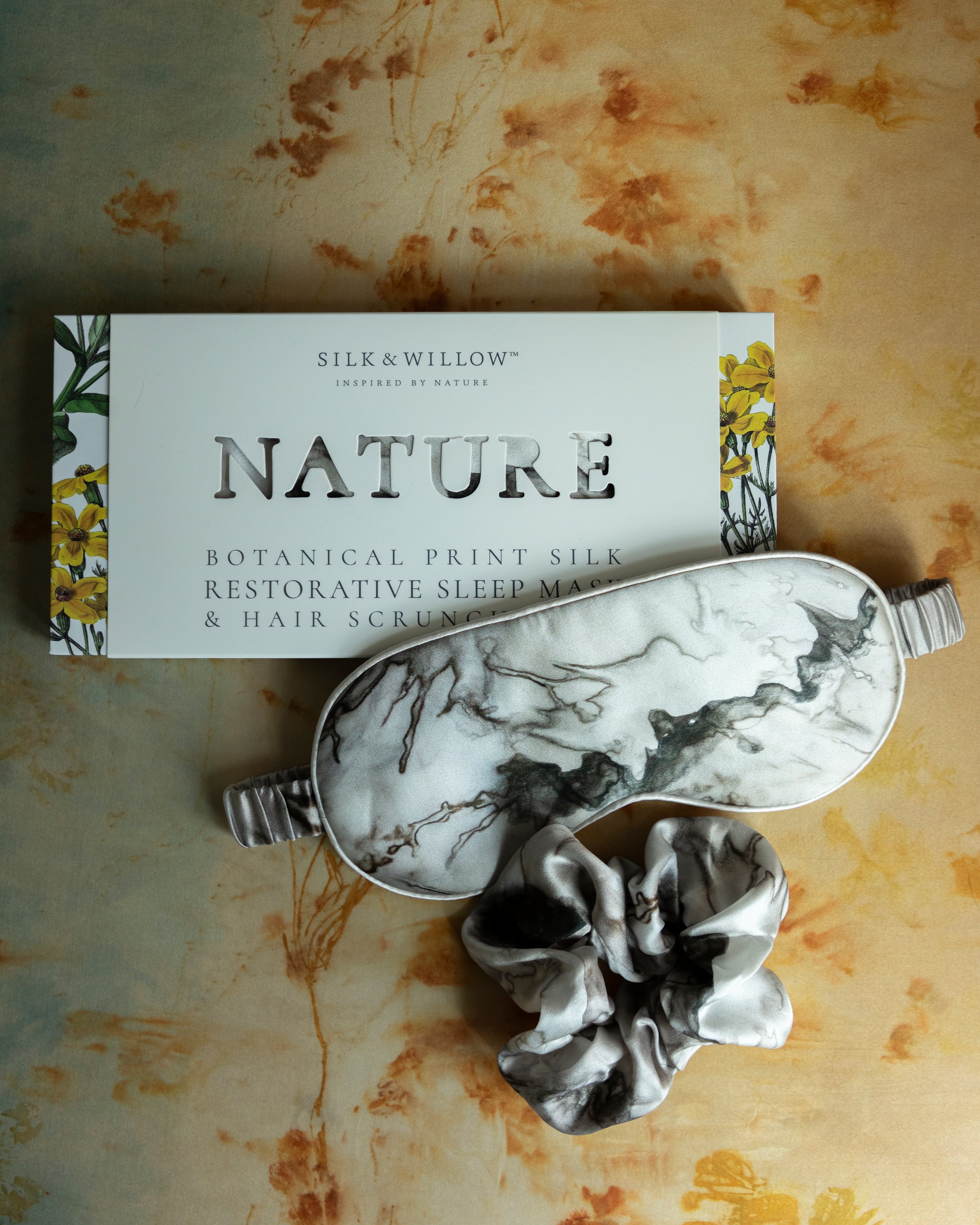 A luxurious silk sleep mask and hair scrunchie set featuring delicate botanical patterns, elegantly displayed in a sustainable gift box, perfect for a sophisticated and eco-conscious touch.