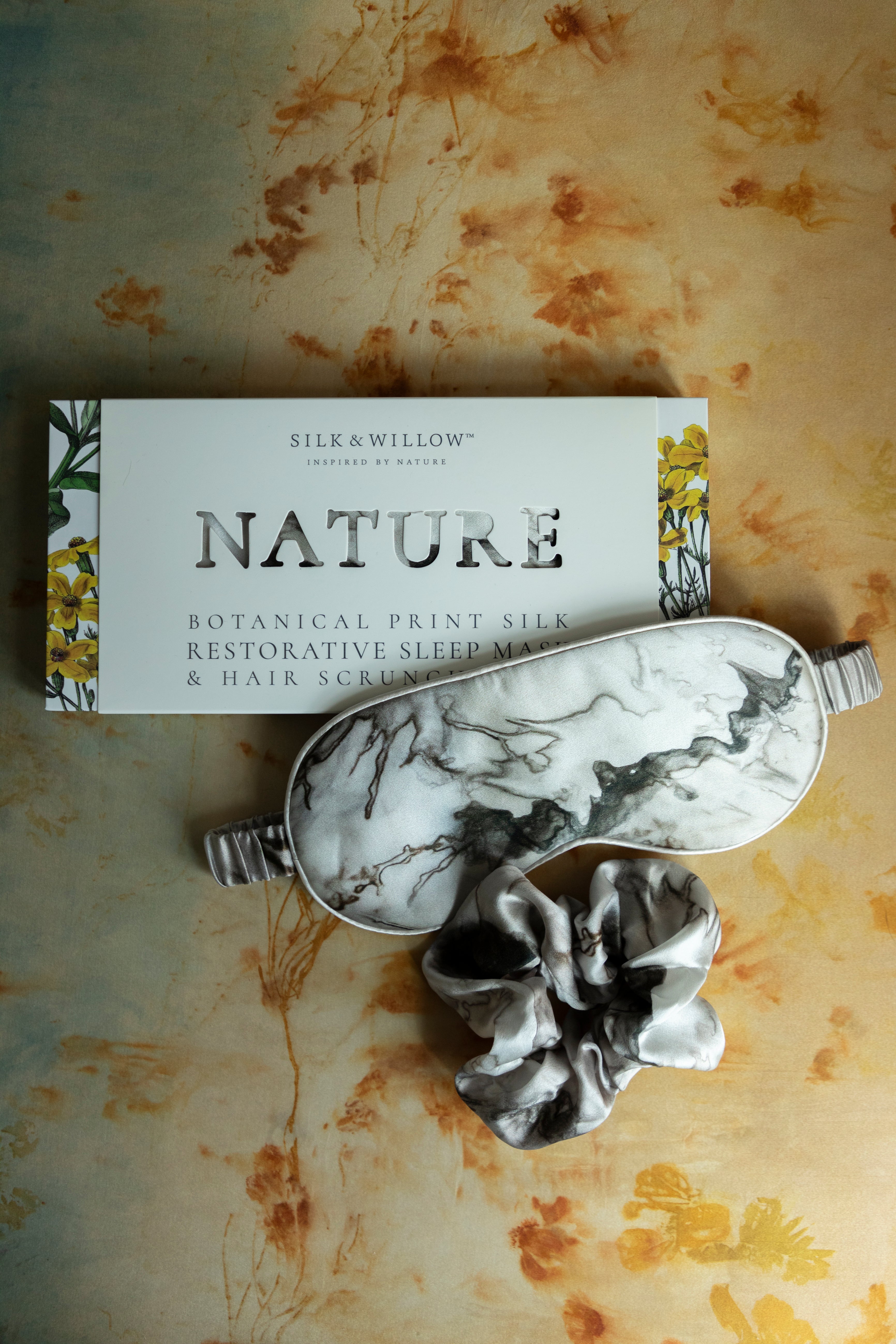 A luxurious silk sleep mask and hair scrunchie set featuring delicate botanical patterns, elegantly displayed in a sustainable gift box, perfect for a sophisticated and eco-conscious touch.