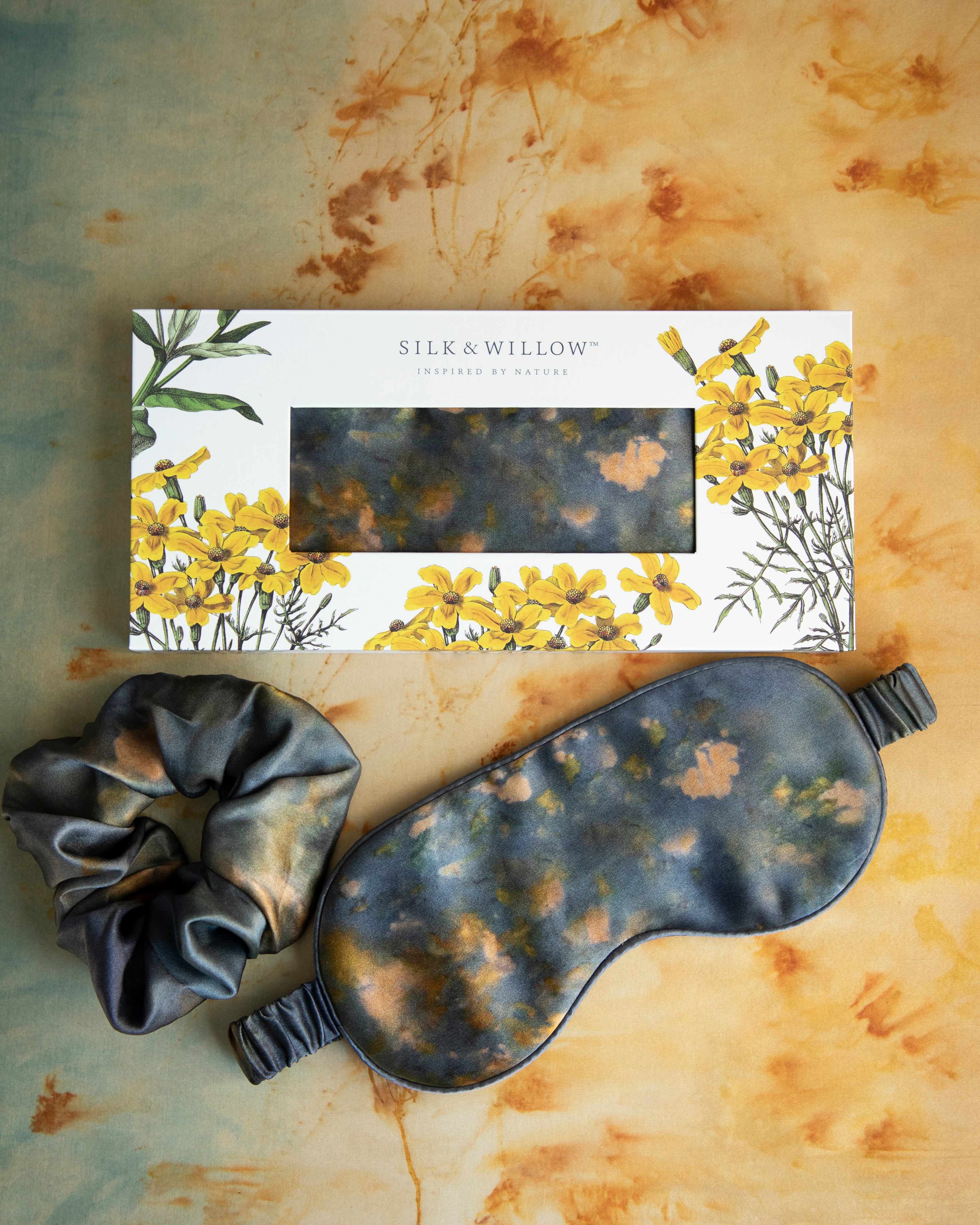 A luxurious silk sleep mask and hair scrunchie set featuring delicate botanical patterns, elegantly displayed in a sustainable gift box, perfect for a sophisticated and eco-conscious touch.