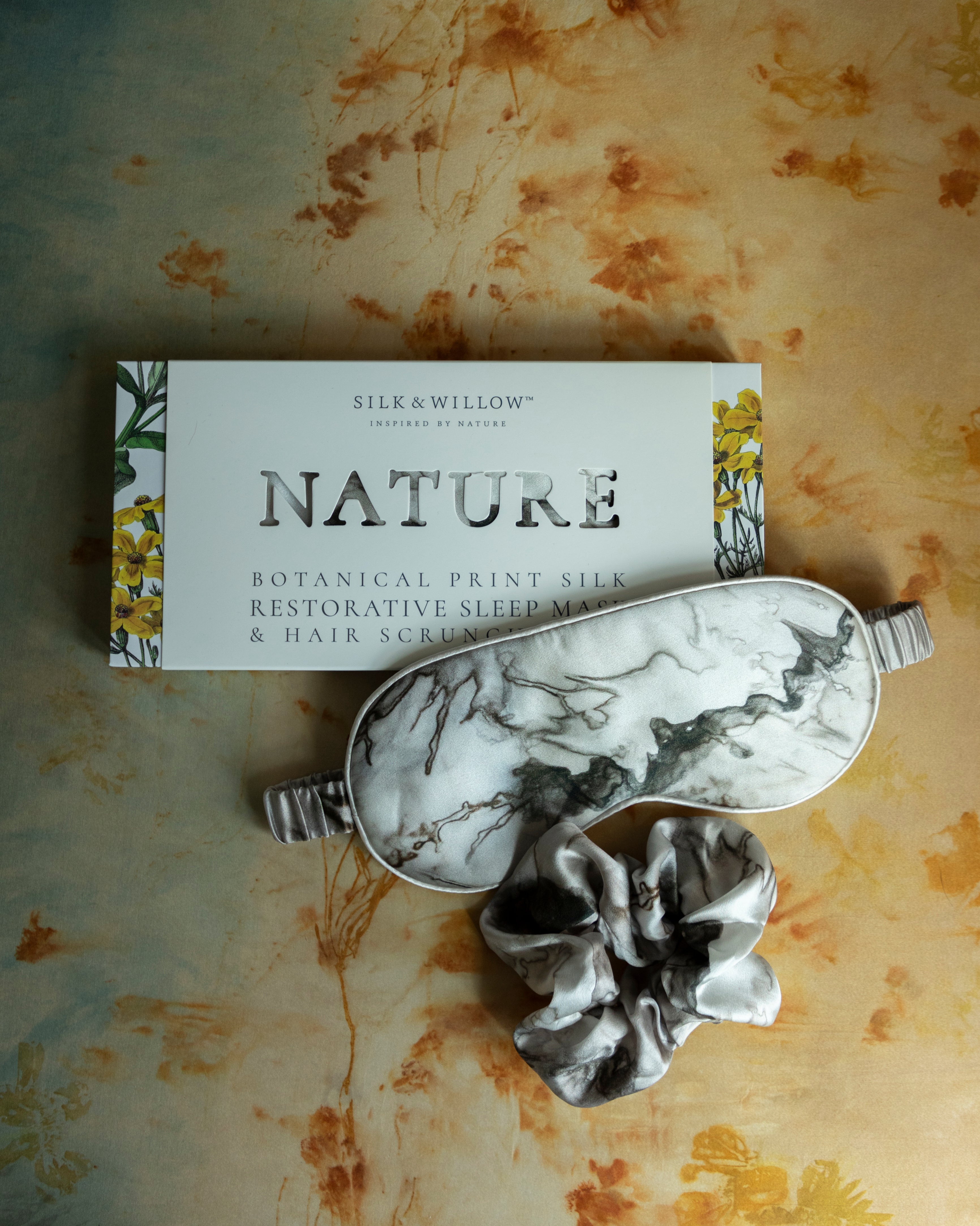 A luxurious silk sleep mask and hair scrunchie set featuring delicate botanical patterns, elegantly displayed in a sustainable gift box, perfect for a sophisticated and eco-conscious touch.