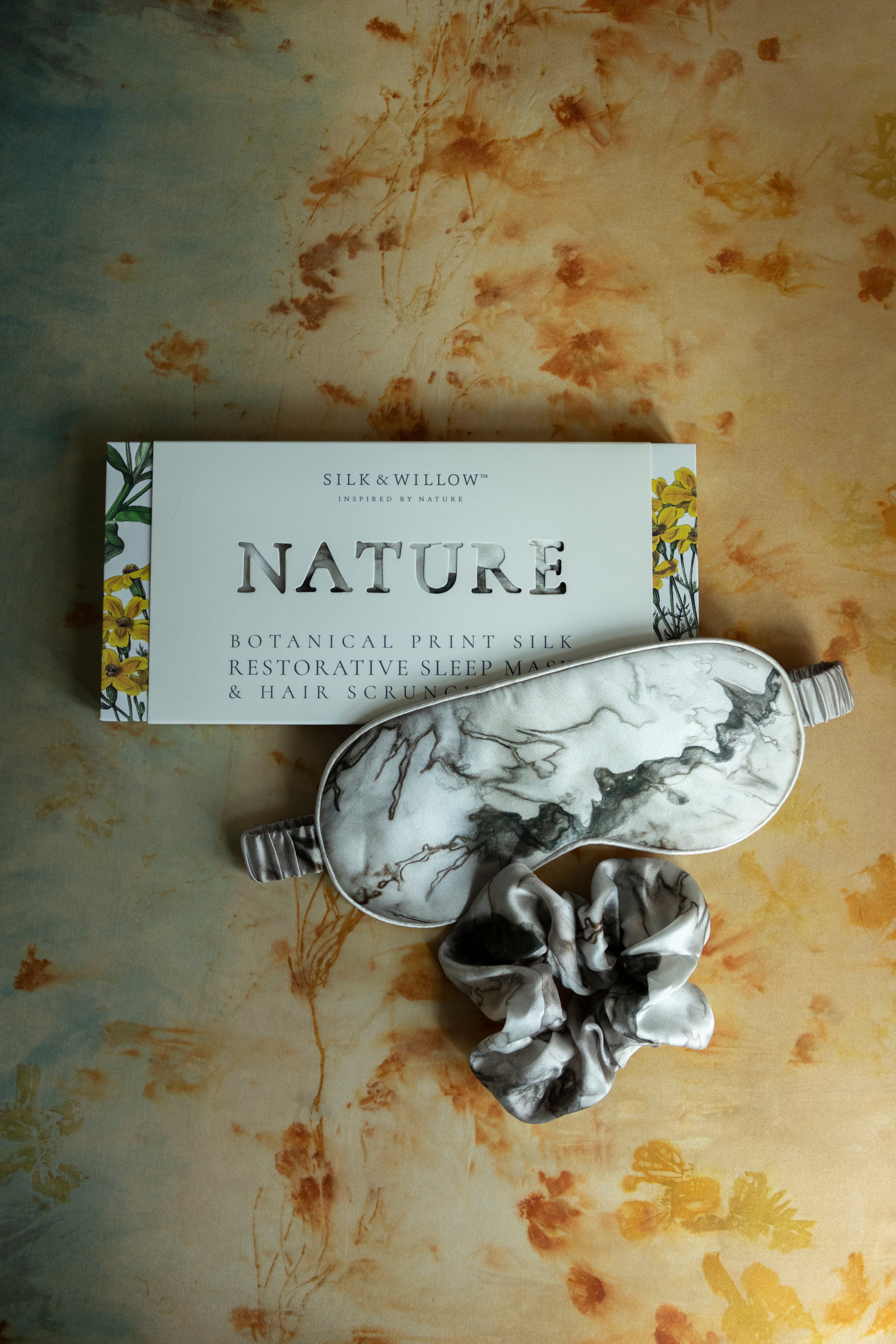 A luxurious silk sleep mask and hair scrunchie set featuring delicate botanical patterns, elegantly displayed in a sustainable gift box, perfect for a sophisticated and eco-conscious touch.
