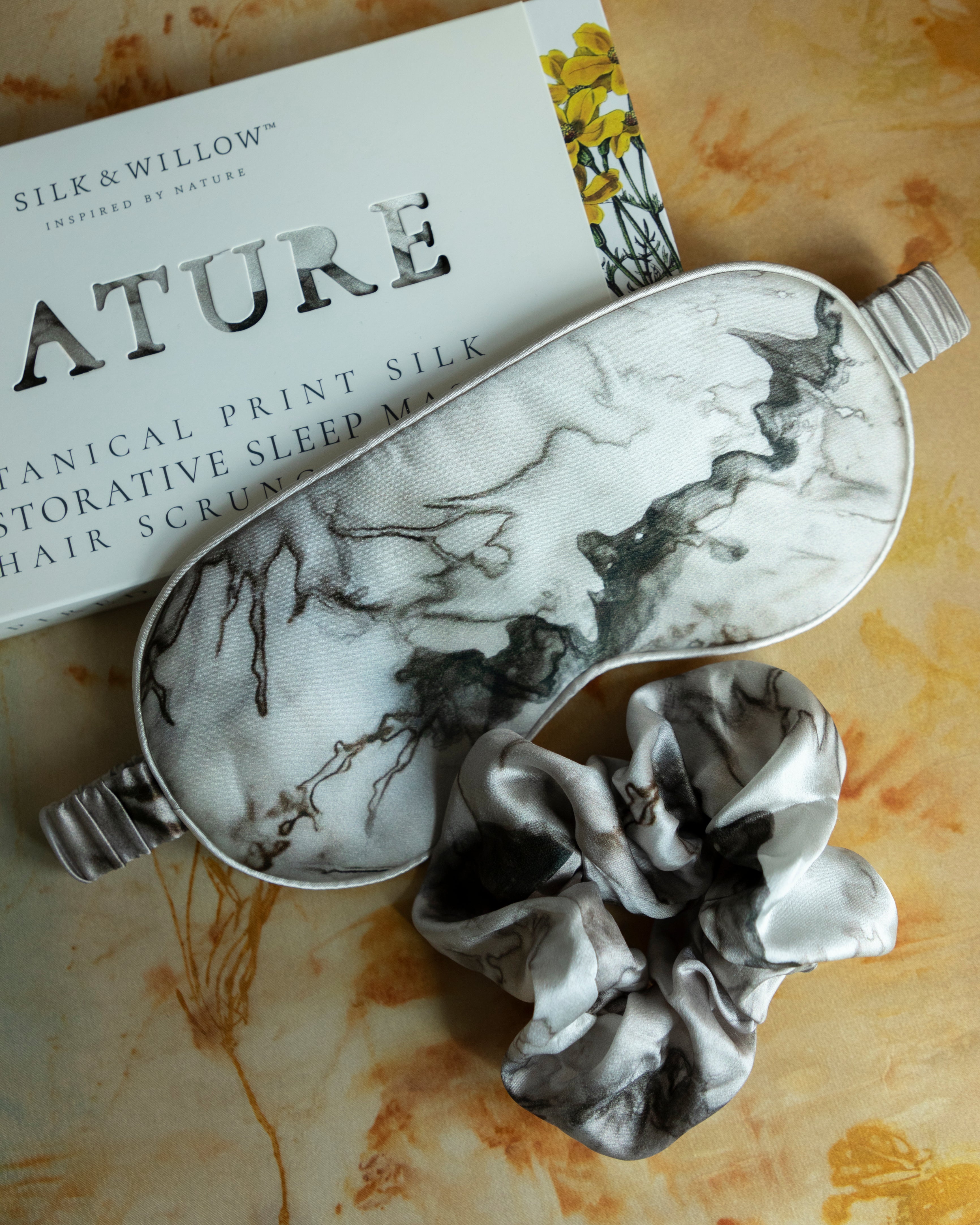 A luxurious silk sleep mask and hair scrunchie set featuring delicate botanical patterns, elegantly displayed in a sustainable gift box, perfect for a sophisticated and eco-conscious touch.