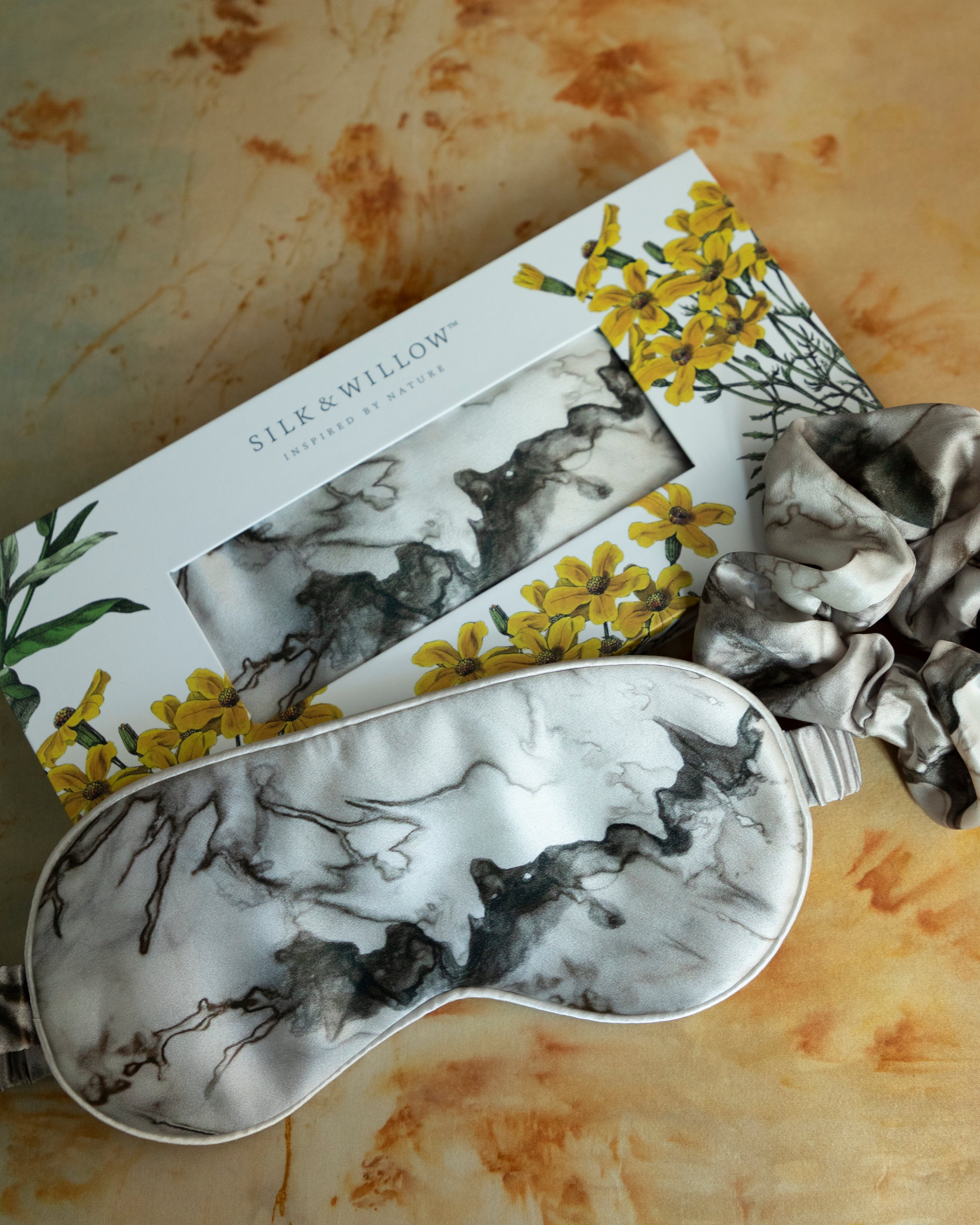 A luxurious silk sleep mask and hair scrunchie set featuring delicate botanical patterns, elegantly displayed in a sustainable gift box, perfect for a sophisticated and eco-conscious touch.
