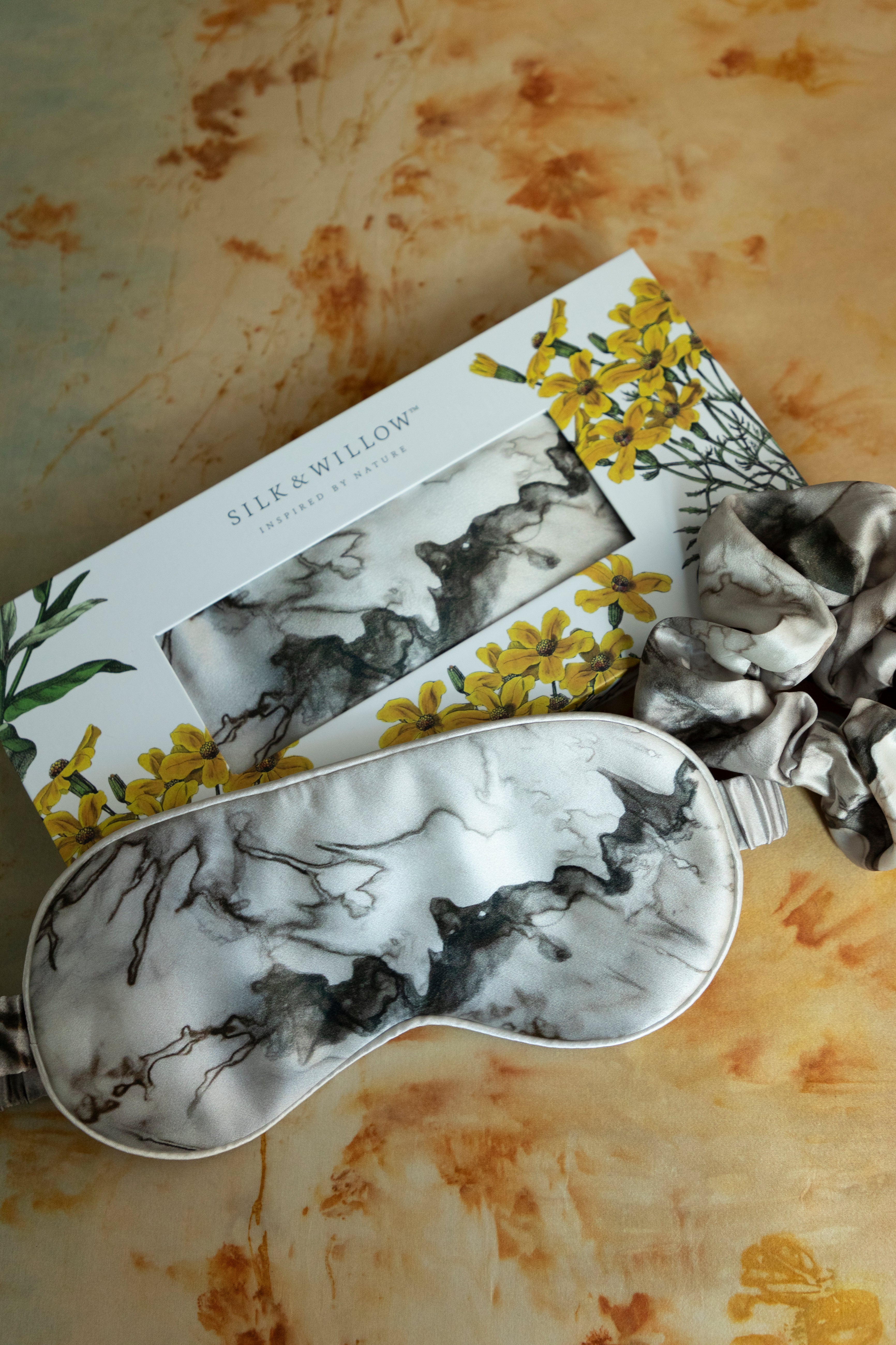 A luxurious silk sleep mask and hair scrunchie set featuring delicate botanical patterns, elegantly displayed in a sustainable gift box, perfect for a sophisticated and eco-conscious touch.