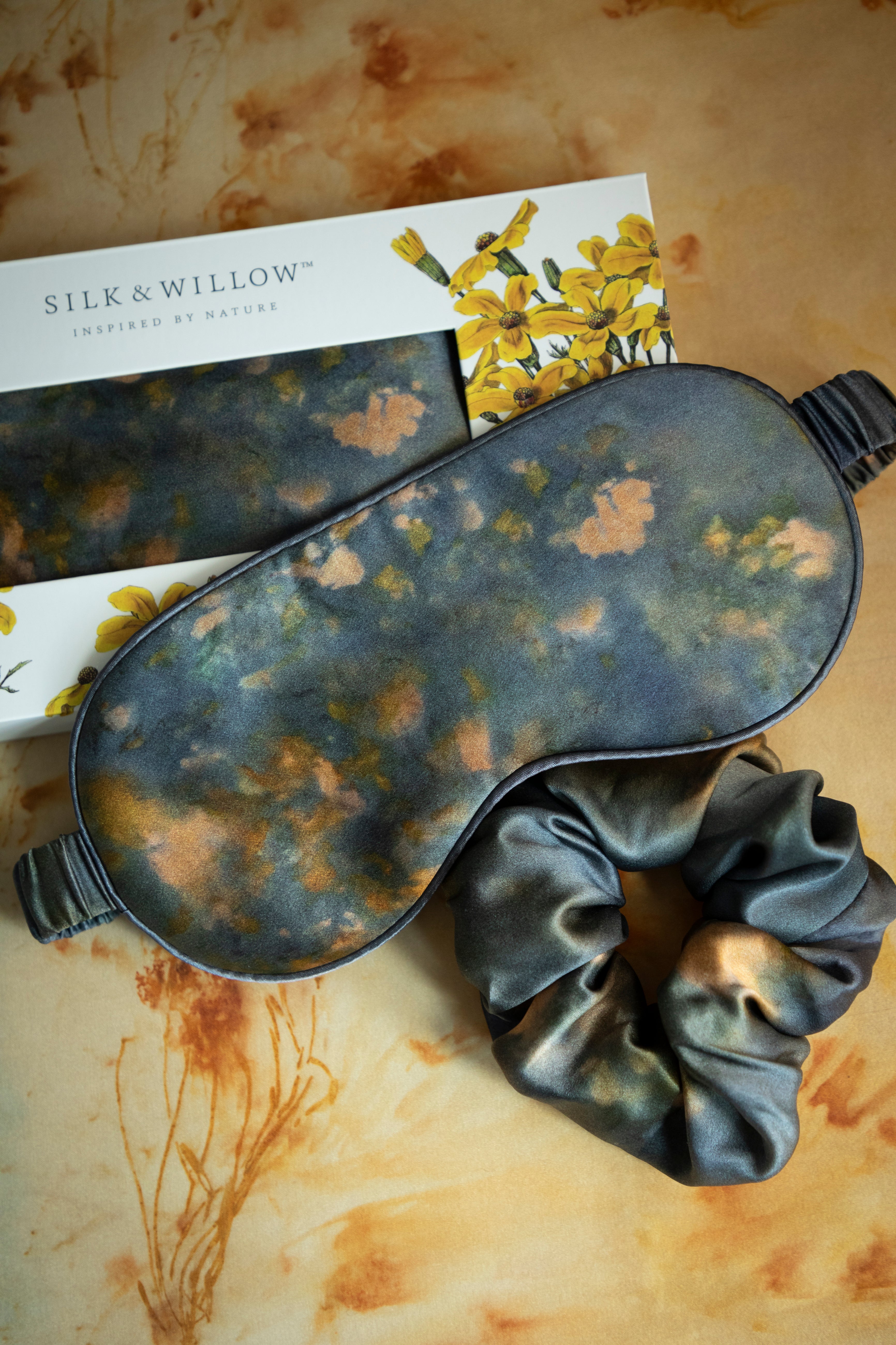 A luxurious silk sleep mask and hair scrunchie set featuring delicate botanical patterns, elegantly displayed in a sustainable gift box, perfect for a sophisticated and eco-conscious touch.