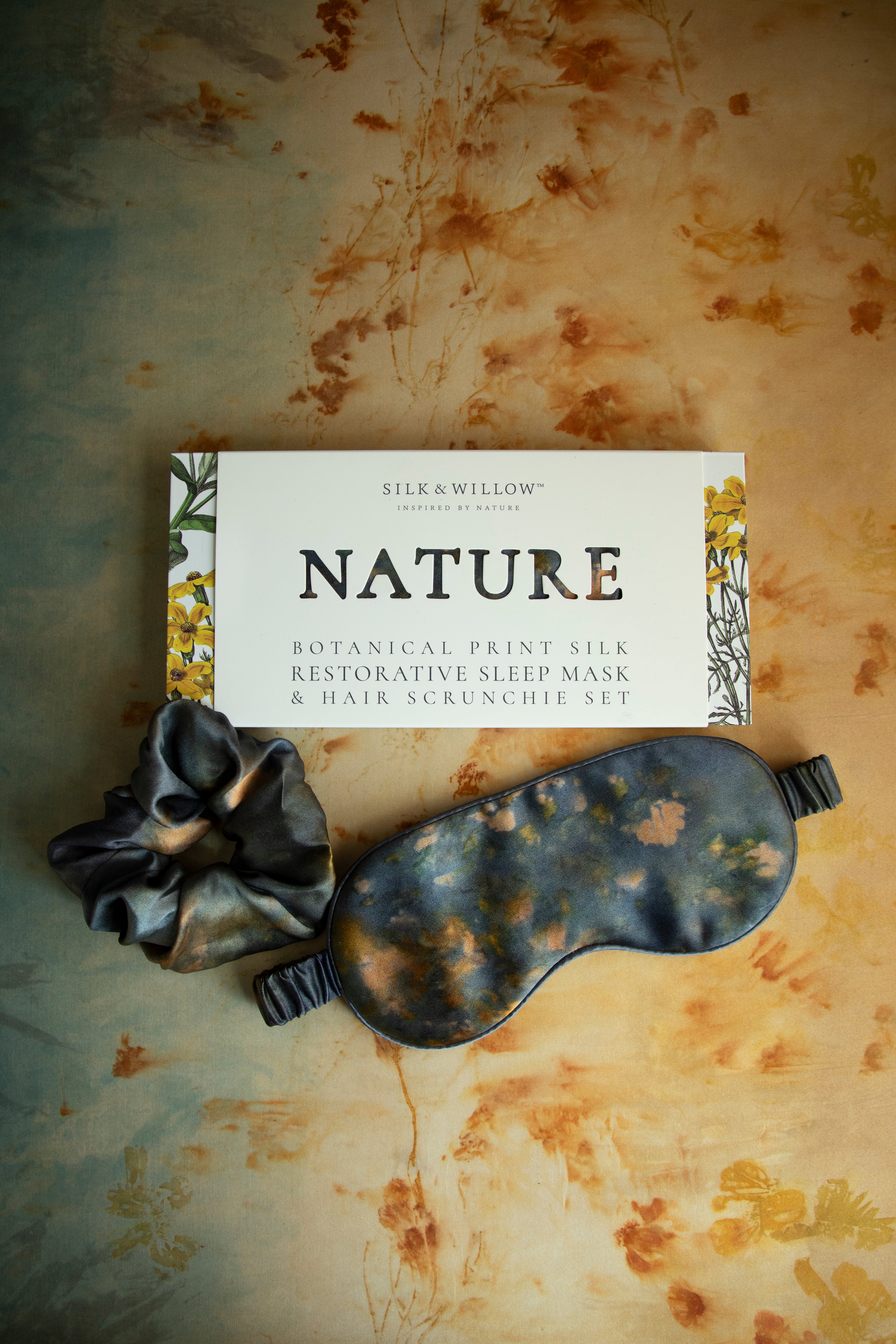A luxurious silk sleep mask and hair scrunchie set featuring delicate botanical patterns, elegantly displayed in a sustainable gift box, perfect for a sophisticated and eco-conscious touch.