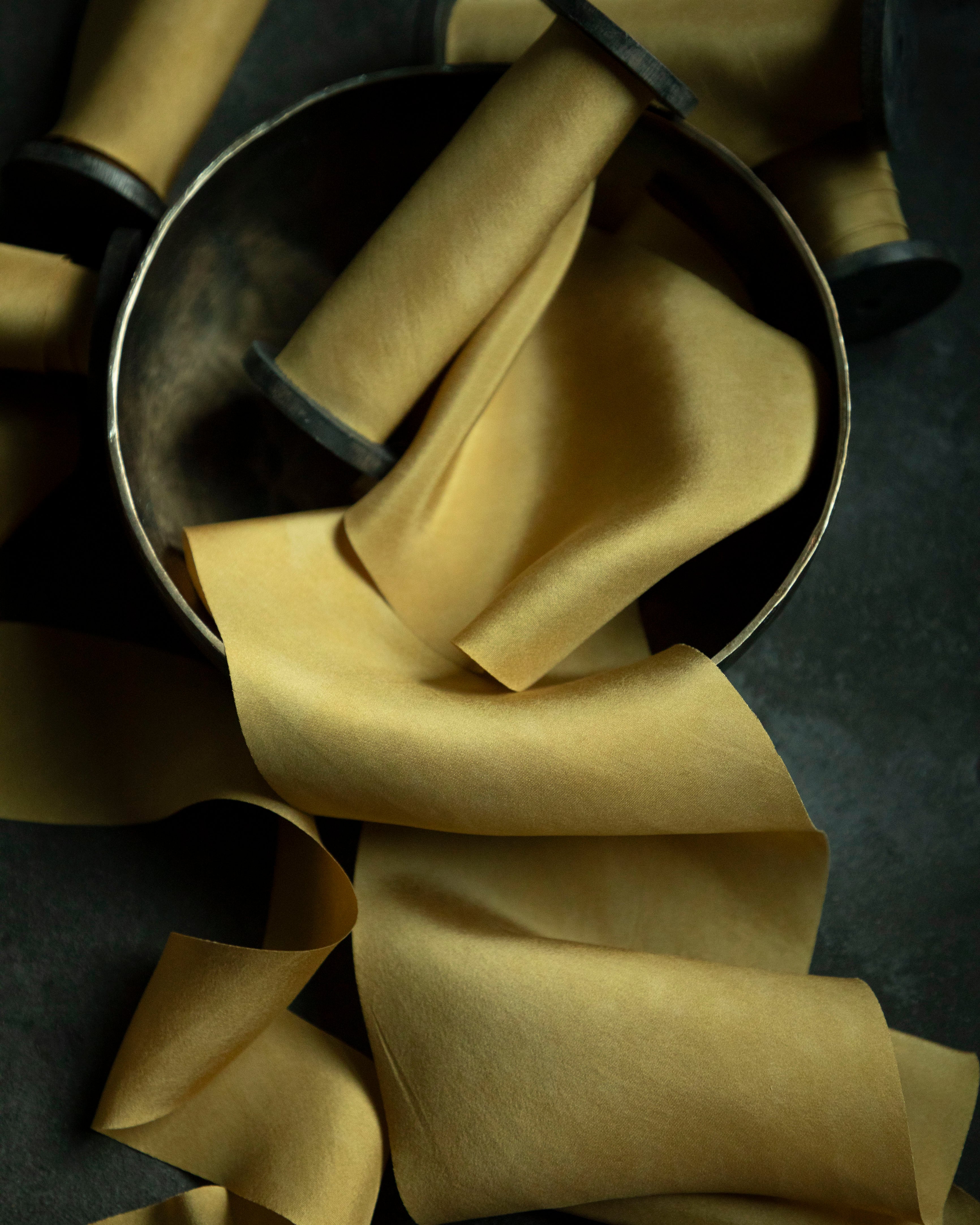 Yellow silk ribbons on a wooden spool on a dark surface with a metal bowl.