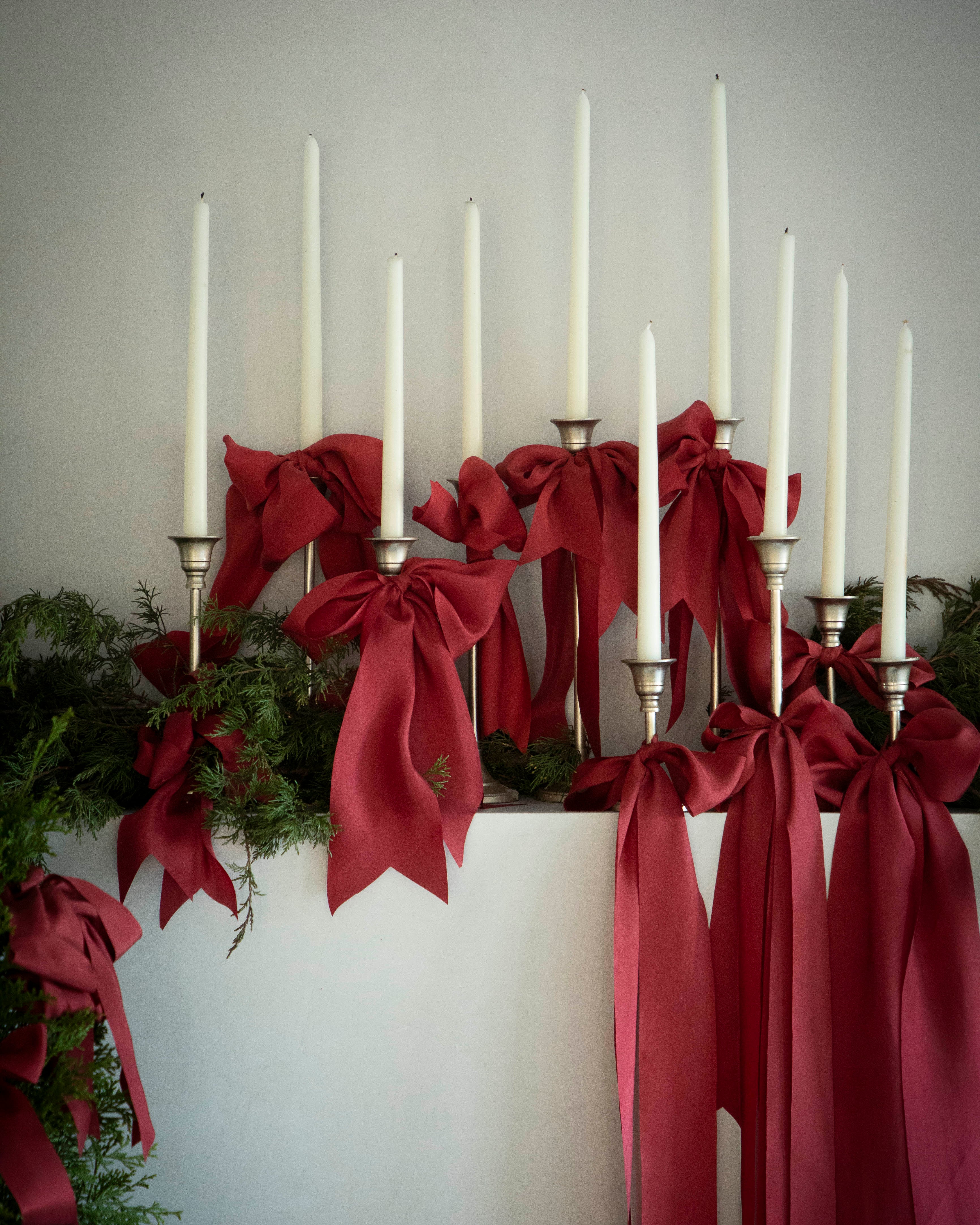chrismas mantel display with candles and red ribbons with winter greenery for a elevated christmas display.