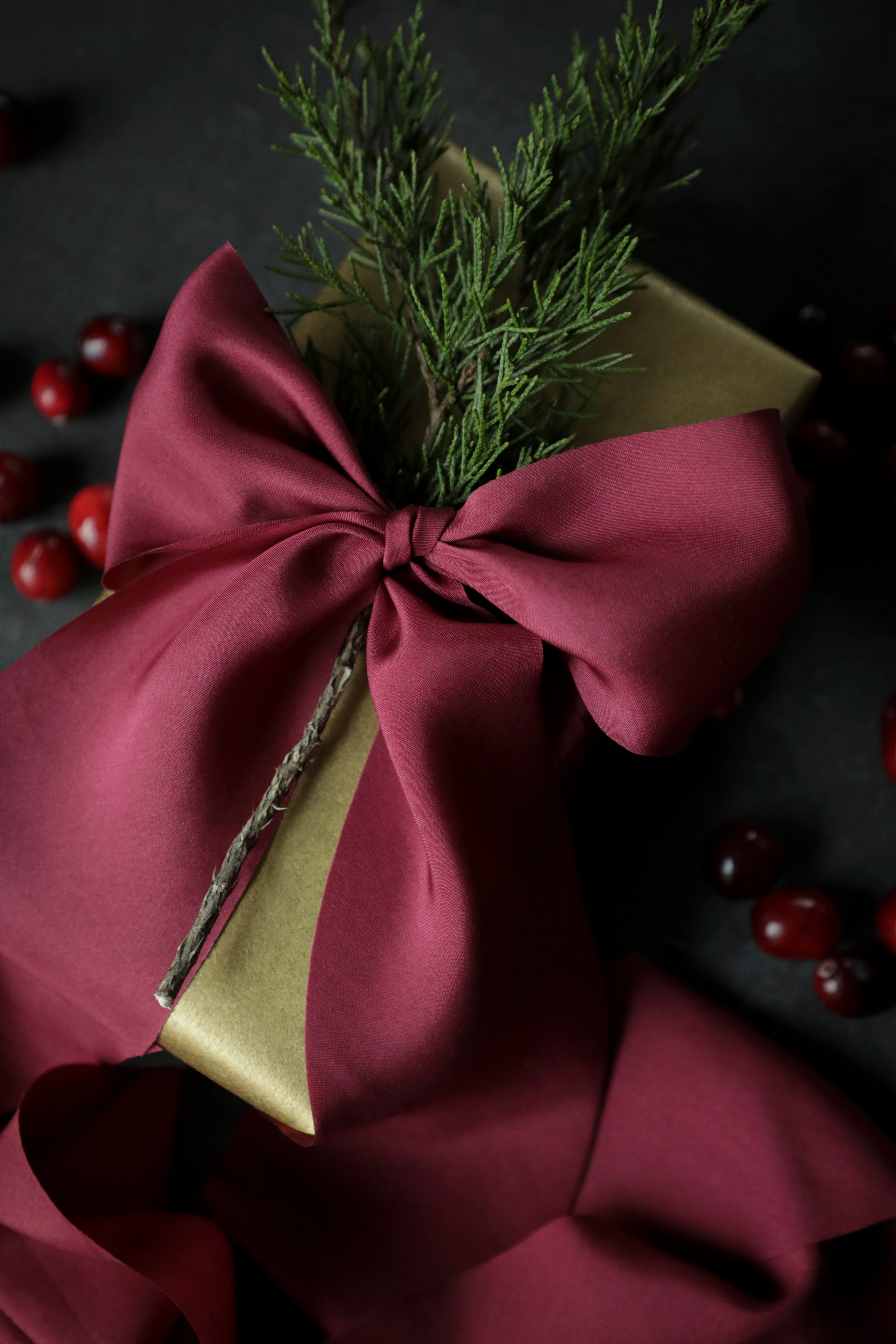 gift wrapping ribbon on a wrapped box on a black background with evergreens and cranberries