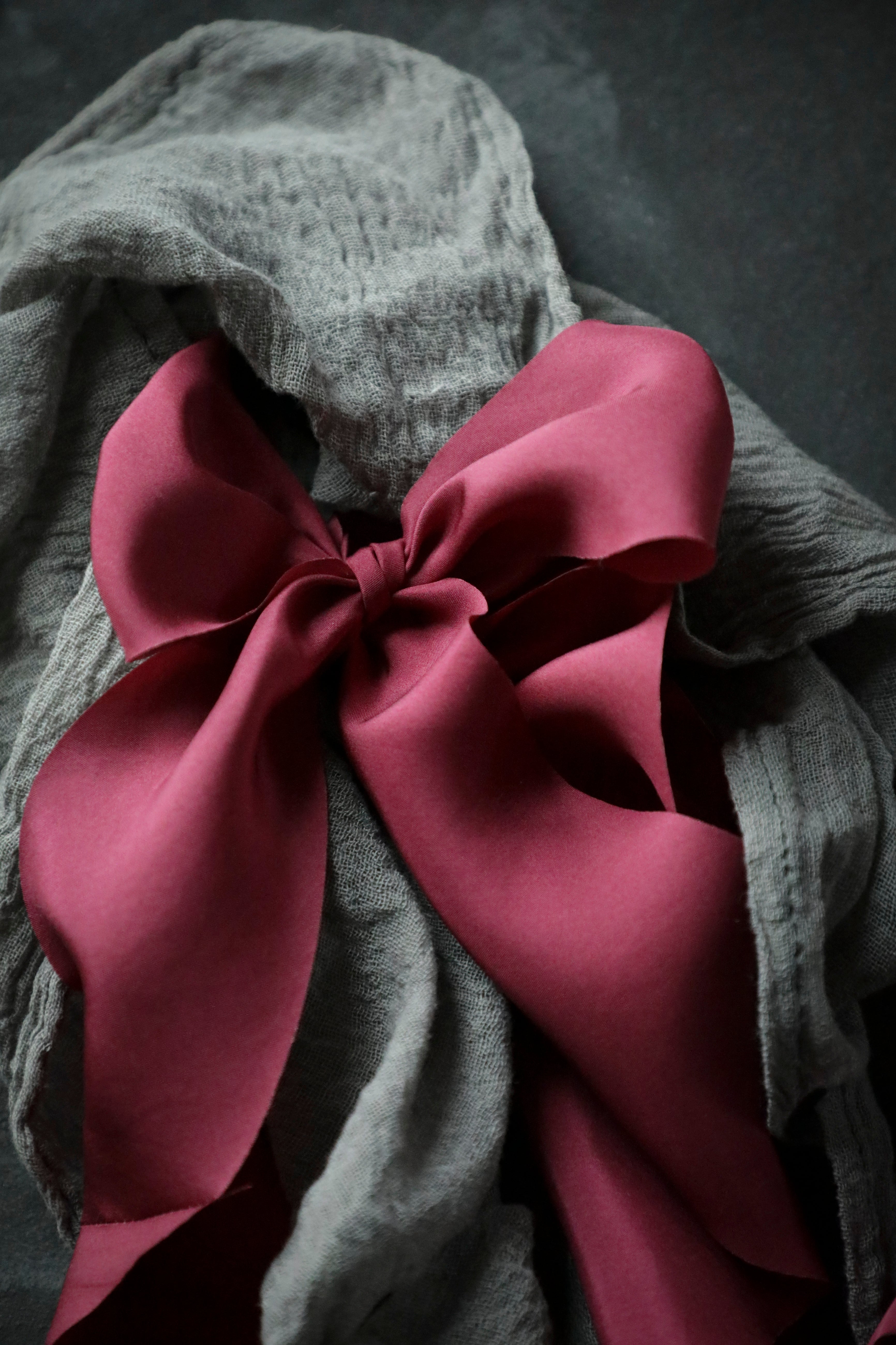 A large, hand-crafted, red silk ribbon laid out on a gray surface, showcasing its soft texture and vibrant color.