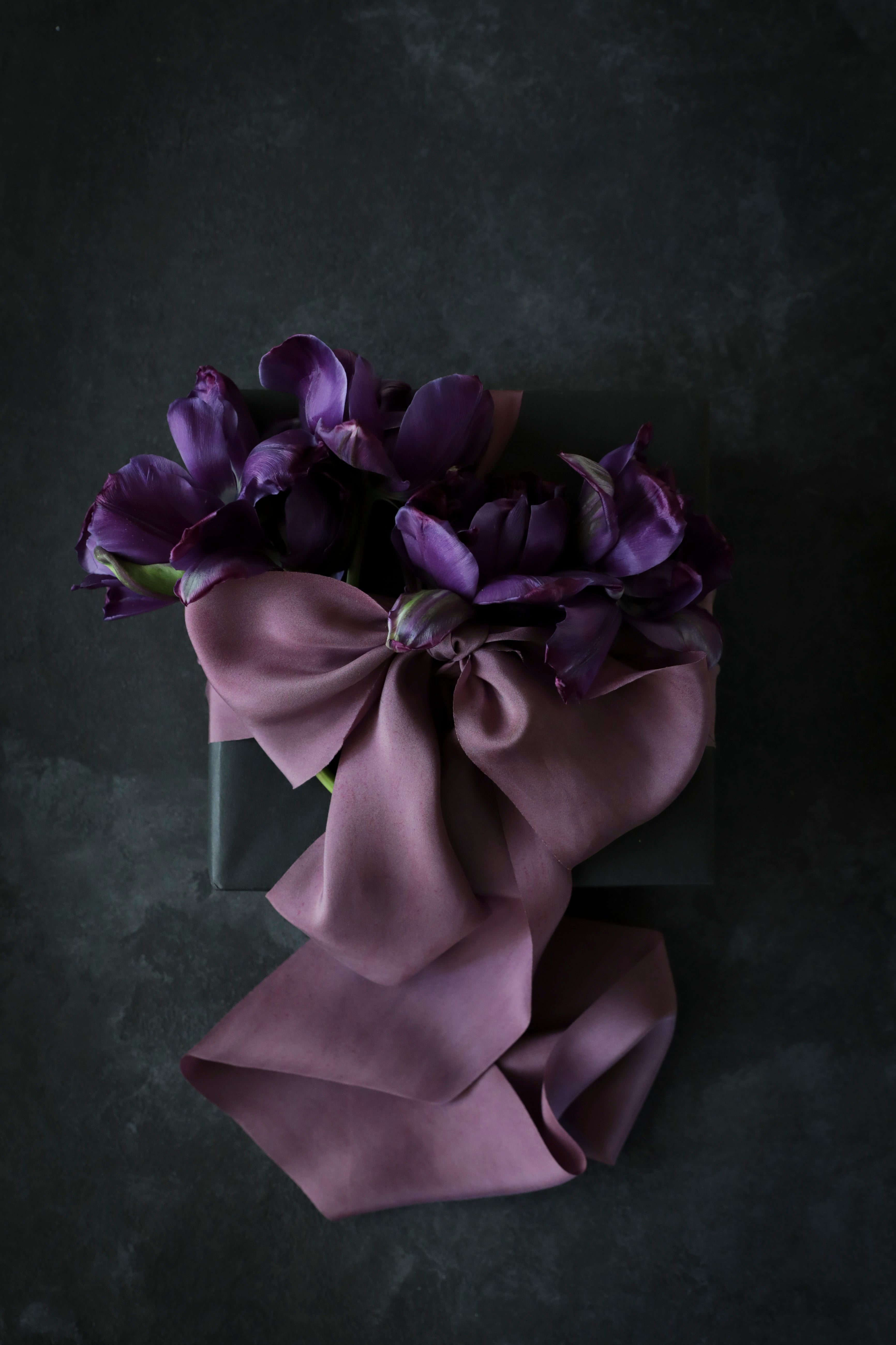 A deep mauve silk ribbon tied in a bow with a marbled pattern and speckles of plant matter, displayed on a dark background.