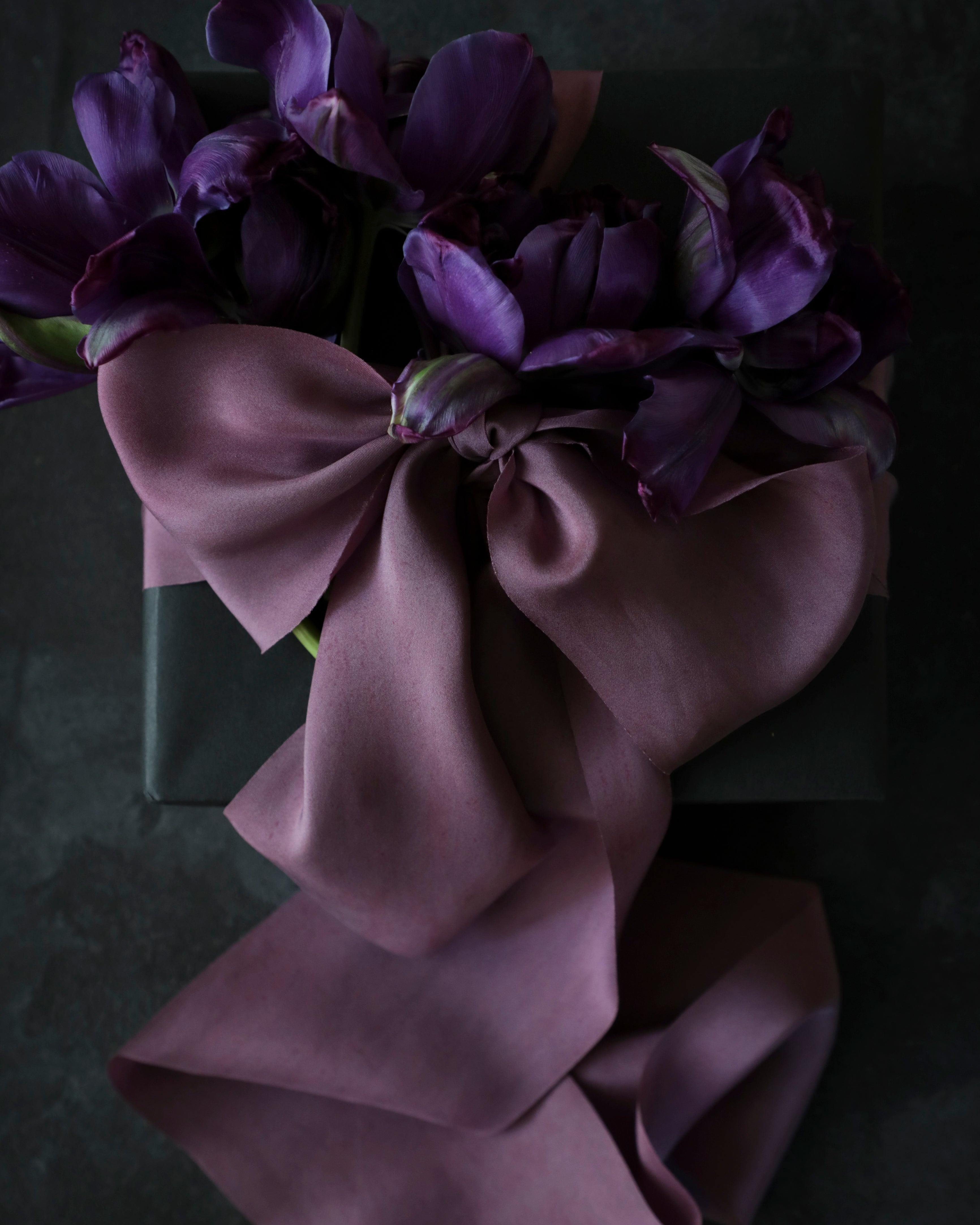 Unique gift wrapping inspiration. gift wrapping with purple silk ribbon bow against a textured black back ground