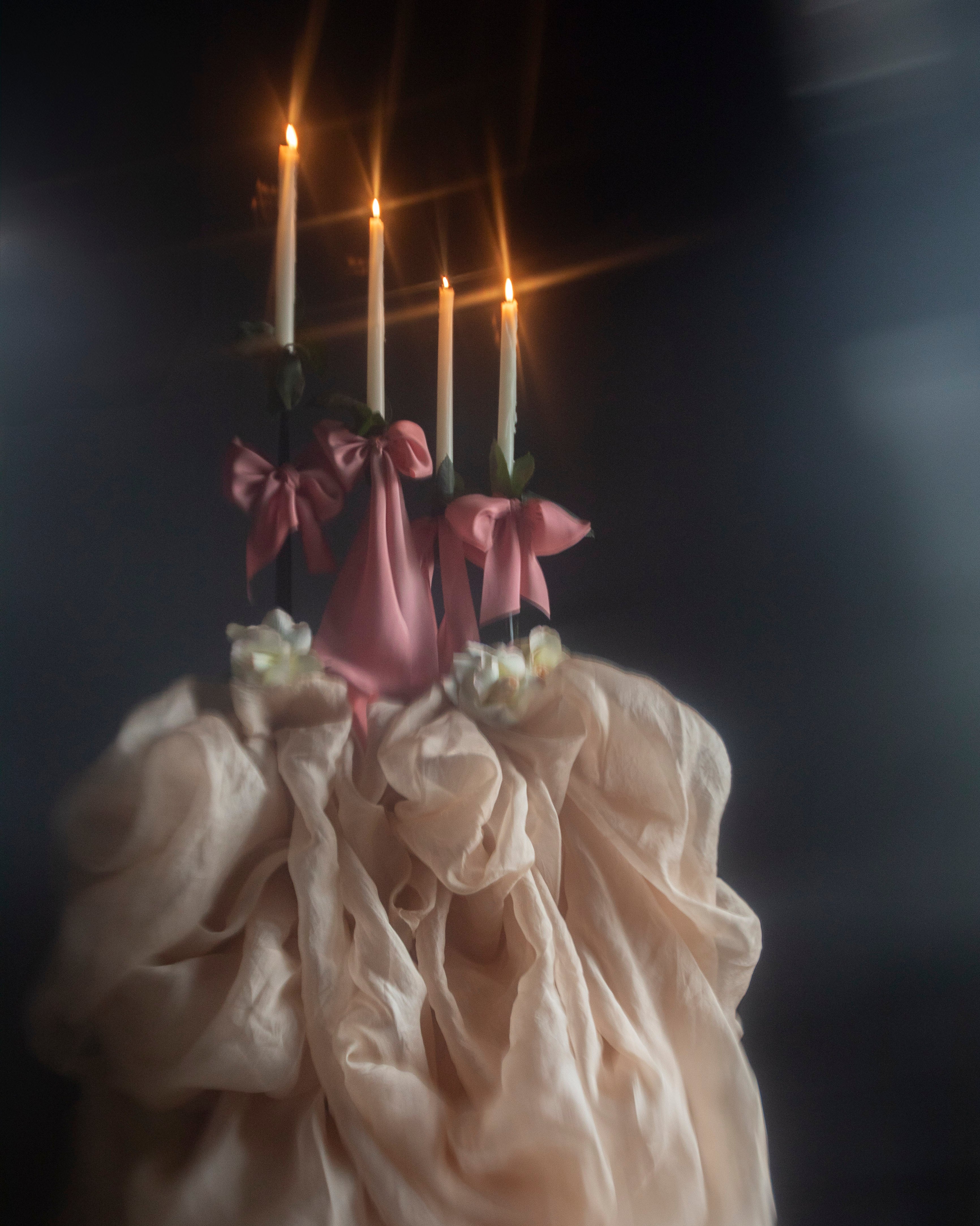 Decorative object with candles and pink ribbons against a dark background
